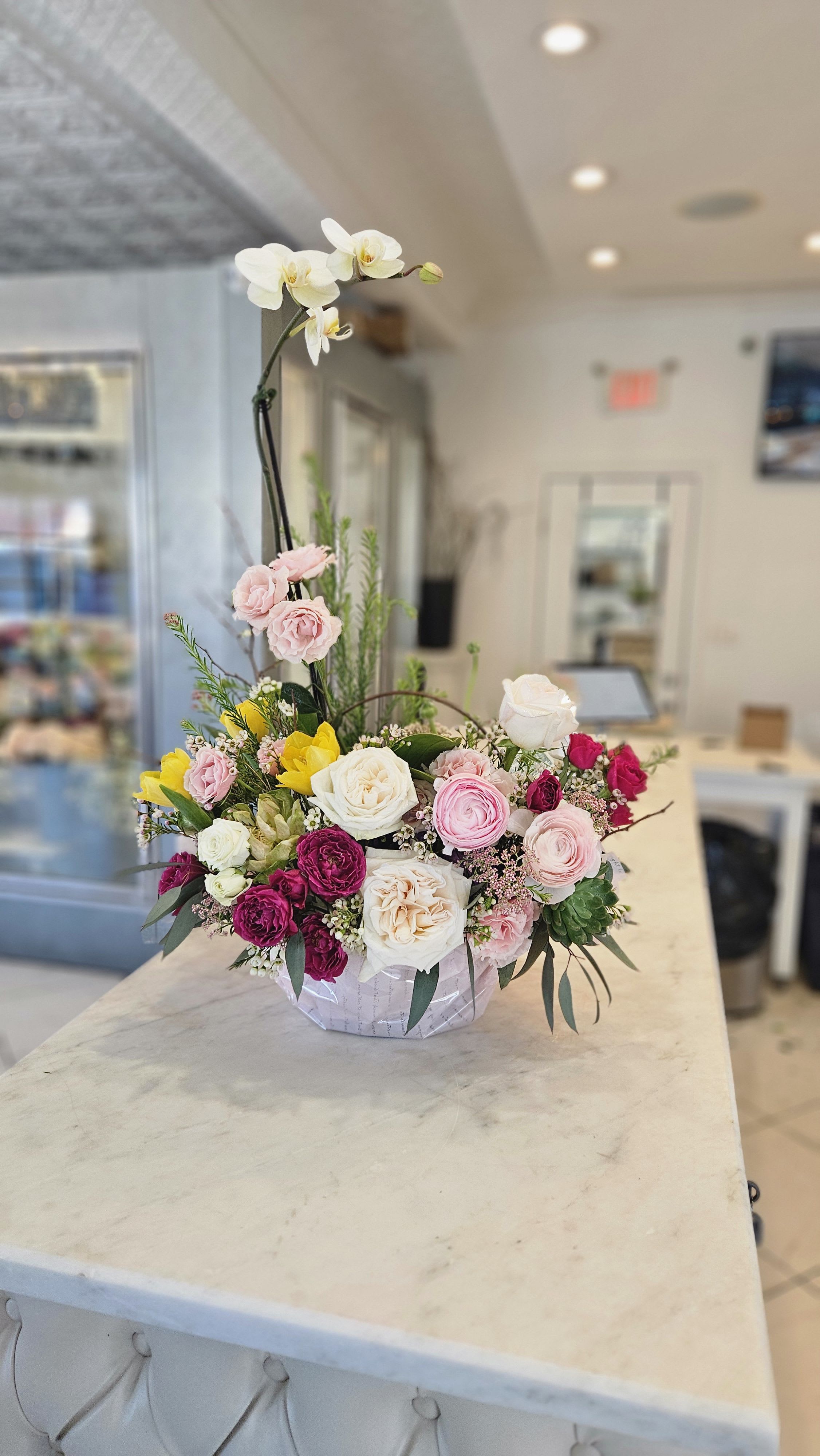 Basket Arrangement - Designer's Choice  - Introducing our stunning Orchid Basket Arrangement, a true showstopper that will elevate any space!    This exquisite arrangement features a beautifully arranged orchid plant nestled in a charming basket, capturing the essence of elegance and grace. Our customers rave about this unique design, not just for its breathtaking beauty, but also for its practicality. After relishing the stunning display, you can easily transplant the orchids into a pot, allowing you to enjoy their vibrant blooms for even longer!  Send this delightful arrangement that beautifully combines elegance and sustainability, and witness the joy radiate across your loved one’s face!  *** PLEASE NOTE - Orchid color and flower color may vary. This is Designer's Choice ***