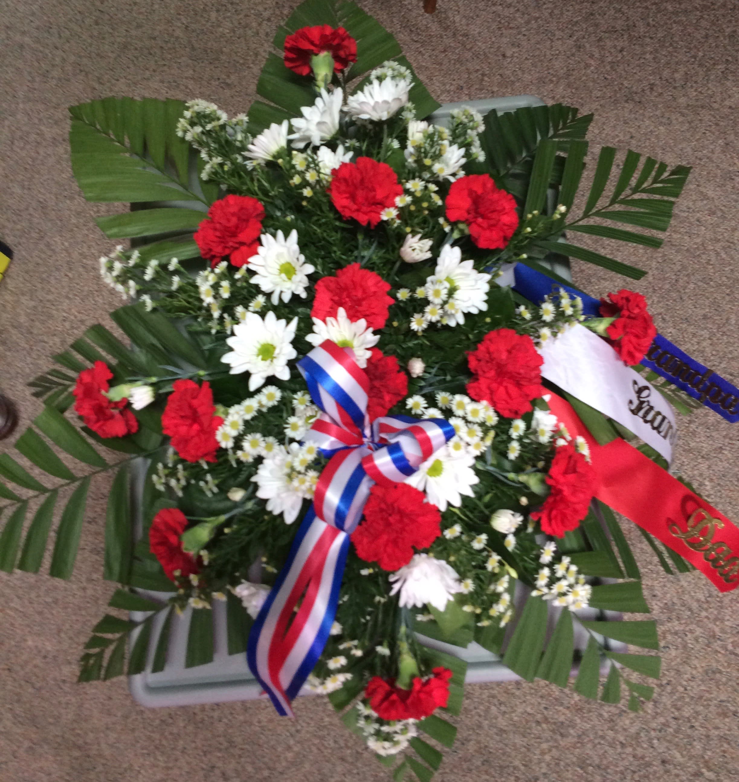 Patriotic Salute Casket Spray Patriotic Salute Casket Spray - This Patriotic Salute is wonderful for someone that served in the Armed Forces. A 1/2 casket spray with carnations, daisies and spray asters surrounding the stately palms and mixed greens. This example has the up-charge of the wording along with the ribbon. If you would like a ribbon & wording, i.e., loving friend, Father, Dear Mother, In-Law, Nephew, etc. Please call us for pricing. thank you.