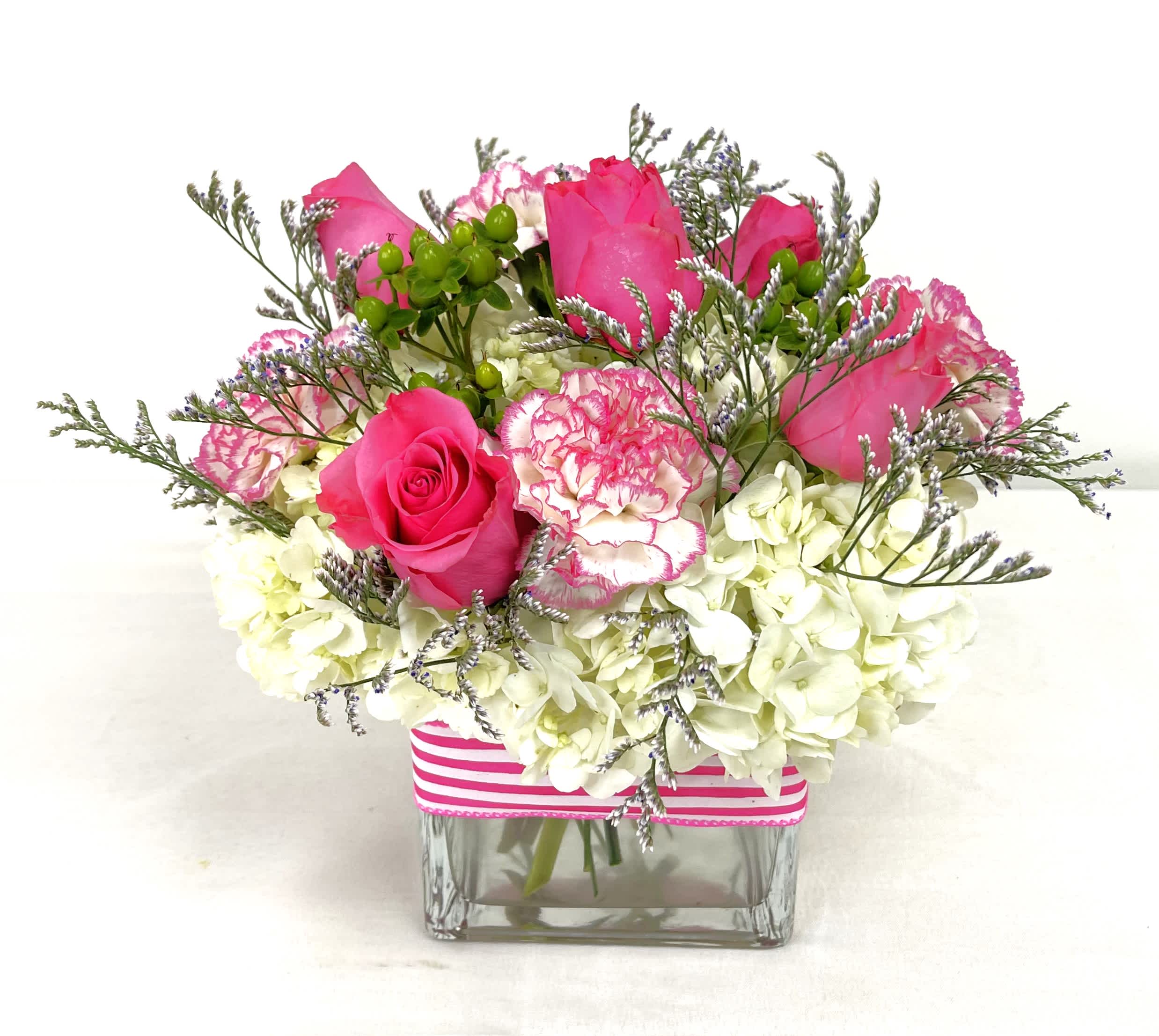 Bright Joy - Beautiful pink and white arrangement in an elegant and clear cube vase. Contains roses, carnations, hydrangeas, hypericum berries, and limonium.