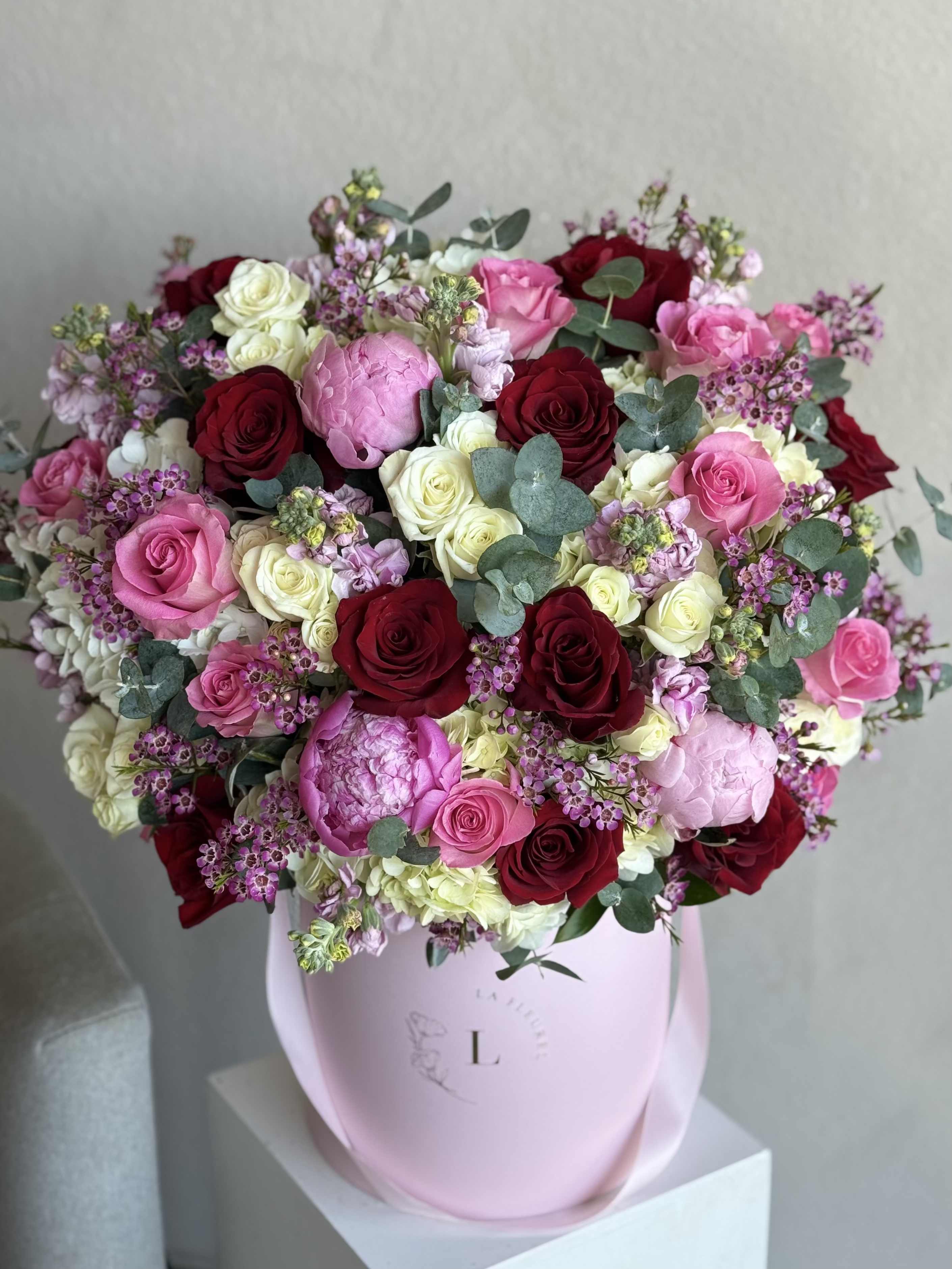 Mom’s Garden with Peonies - A lush and elegant arrangement featuring red roses, pink peonies, wax flower, eucalyptus, and seasonal blooms—all nestled in a soft pink box. Designed to capture the warmth, beauty, and love only a mother can give.
