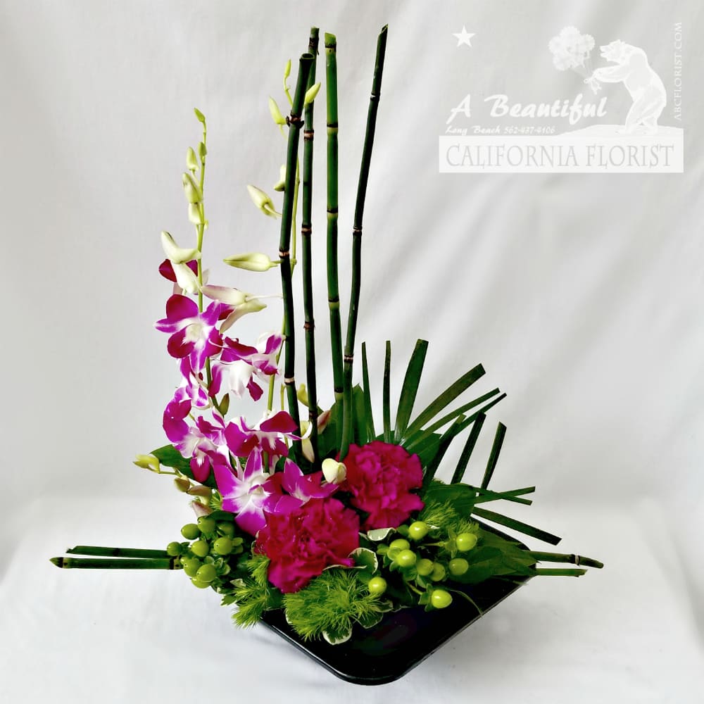 Trade Wind - The Trade Wind - With this tropical design of lavender dendrobium orchids, trailing up miniature bamboo shoots, verdant tropical foliage in jet black container. Transport your recipient to a leisurely fun day of an Island paradise,... at least that is the feeling they'll get when they receive this beautiful arrangement. Trade Wind, another ABC Florist EXCLUSIVE! 