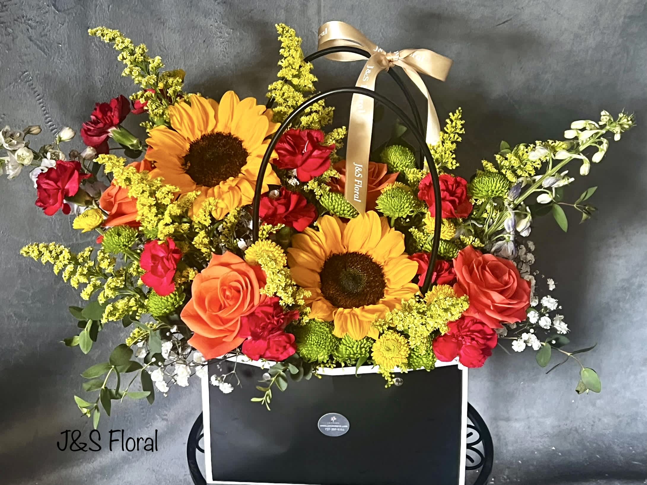 Surprise Me  - Introducing our design Surprise Me! Beautifully arranged with sunflowers, roses , delphiniums, mini carnations, fillers and greenery in a unique black bag. The perfect gift for any occasion!