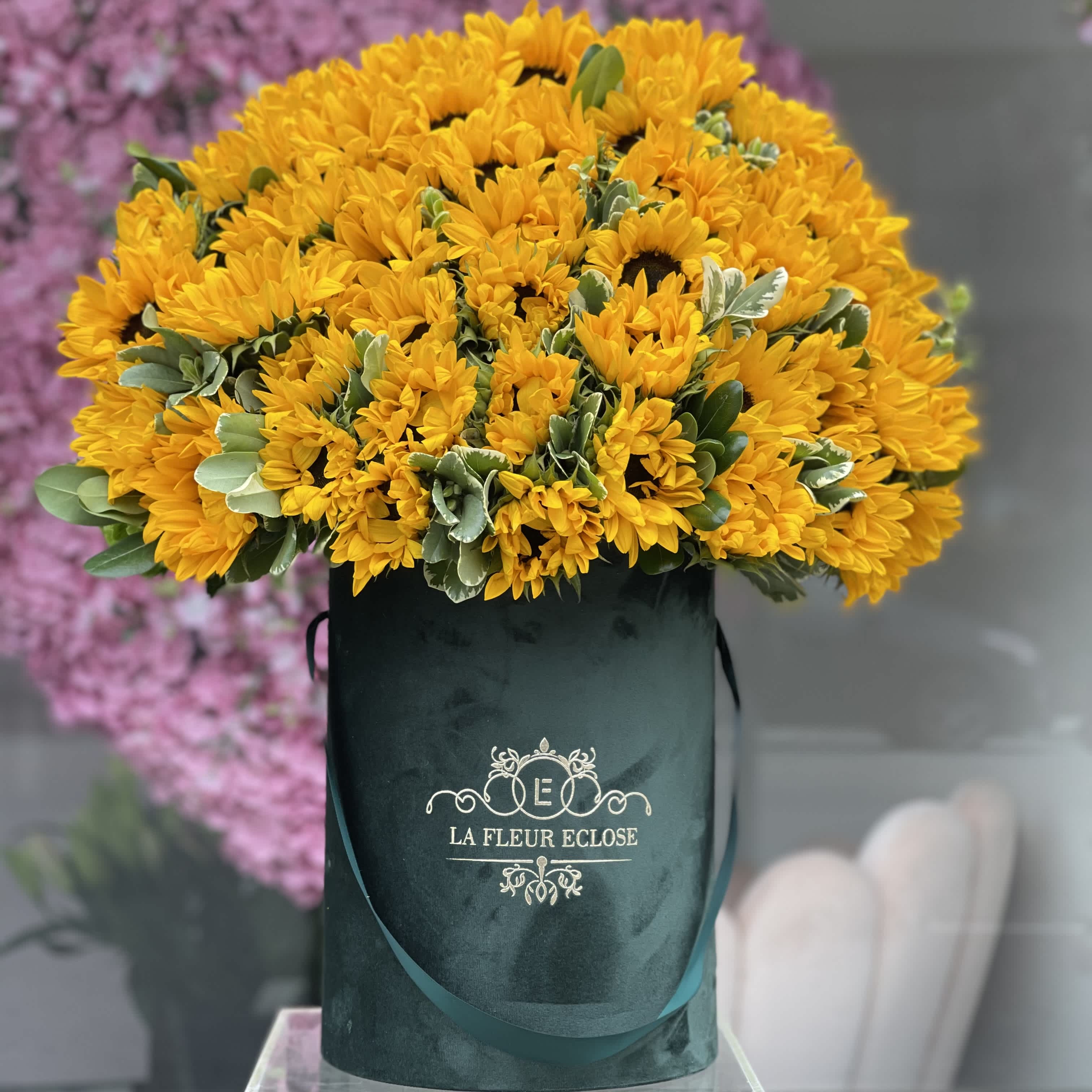 Sunflowers For Mom - This flower arrangement features bright and cheerful sunflowers elegantly presented in a pristine green velvet box. The vibrant yellow petals of the sunflowers contrast beautifully against the vibrant green velvet, creating a visually striking and luxurious display.   The overall aesthetic is both charming and stylish, offering a blend of natural beauty and opulent design.