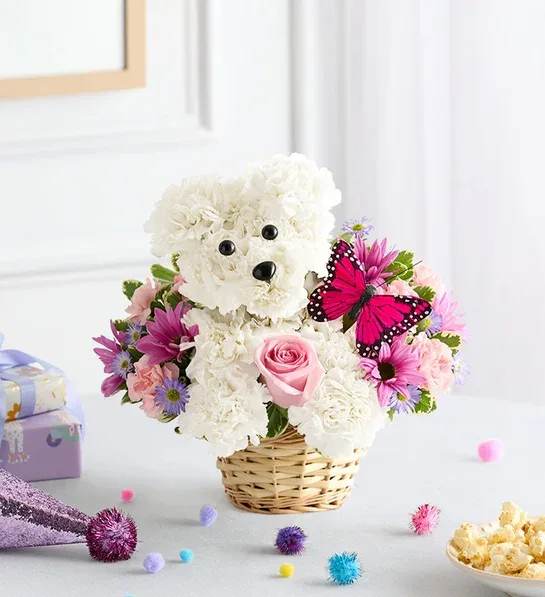 Precious Pup™ Precious Pup™ - EXCLUSIVE Our truly original 3D pup is a precious Mother’s Day surprise. Crafted from white carnations, with sweet pink blooms all around and a butterfly accent, this canine creation is designed in a dog bed basket. For more happy wishes, add our festive “Happy Mother’s Day” balloon. One-sided, 3D arrangement with white carnations crafted in the shape of a dog complete with eyes and nose; surrounded by a mix of pink roses, light pink mini carnations and purple monte casino; accented with assorted greenery and butterfly pick Arrangement measures approximately 11"H x 11"W Artistically designed in our lined wicker pet basket; measures 3.5"H x 5"D Our florists hand-design each arrangement, so colors and varieties may vary due to local availability Add to her gift: Mother’s Day Mylar balloon measures 18"D; design may vary due to local availability