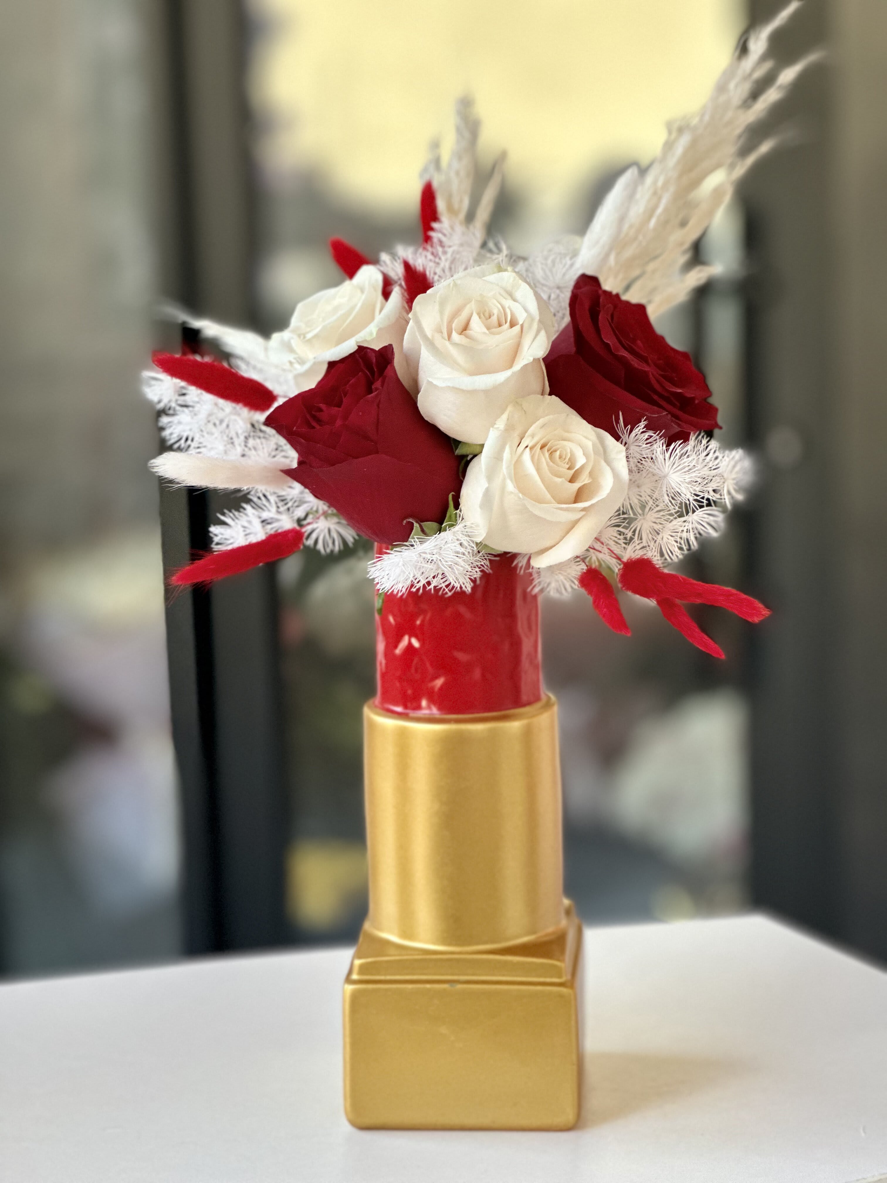 Lipstick Galore - Introducing a stunning arrangement of red and white roses in a lipstick vase, which adds a touch of modern elegance, making it a chic addition to any home decor. This arrangement effortlessly elevates any space with its vibrant color and timeless beauty. 