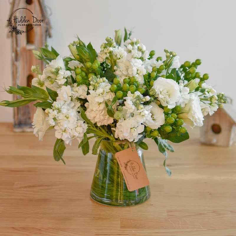 Morning Mist -   At the heart of this arrangement, the pristine white lisianthus showcases its delicate petals with grace and elegance. Its timeless beauty symbolizes purity and simplicity, adding an element of serenity to the composition.  Complementing the lisianthus, the elegant white stock flowers make a stunning impression. Their blossoms exude a captivating fragrance that fills the air with a sweet and alluring scent. The gorgeous aroma wafts through the room, creating an immersive experience that captivates the senses.  Nestled within the clear glass vase, the &quot;Morning Mist&quot; arrangement becomes a mesmerizing centerpiece that allows the lisianthus's delicate beauty and the stock flowers' captivating fragrance to shine. The vase's transparency accentuates the arrangement's ethereal nature, creating a sense of floating serenity as if misty morning dew gently embraces the blossoms.  The &quot;Morning Mist&quot; arrangement is an exquisite choice for those seeking an infusion of elegance and tranquility for any occasion. Whether it's a heartfelt gesture to a loved one, a celebration of life's milestones, or a moment of personal serenity, this arrangement will infuse the surroundings with joy and peacefulness, creating a lasting memory for all who experience it.  