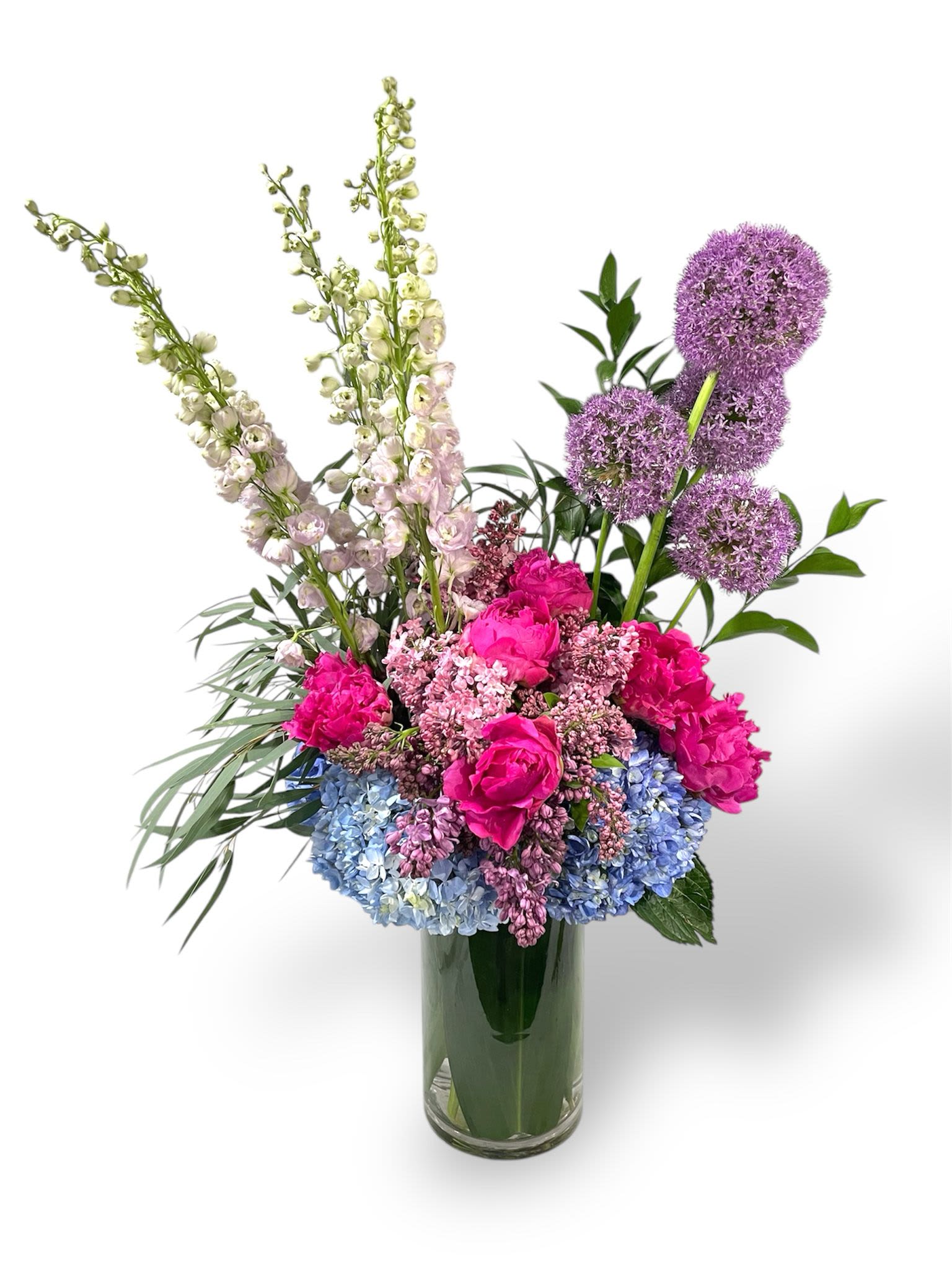 Daphne Daphne - This marvelous arrangement has alliums, pink delphiniums, peonies, lilacs, hydrangeas, and greens in a 6 x 12 cylinder glass vase.