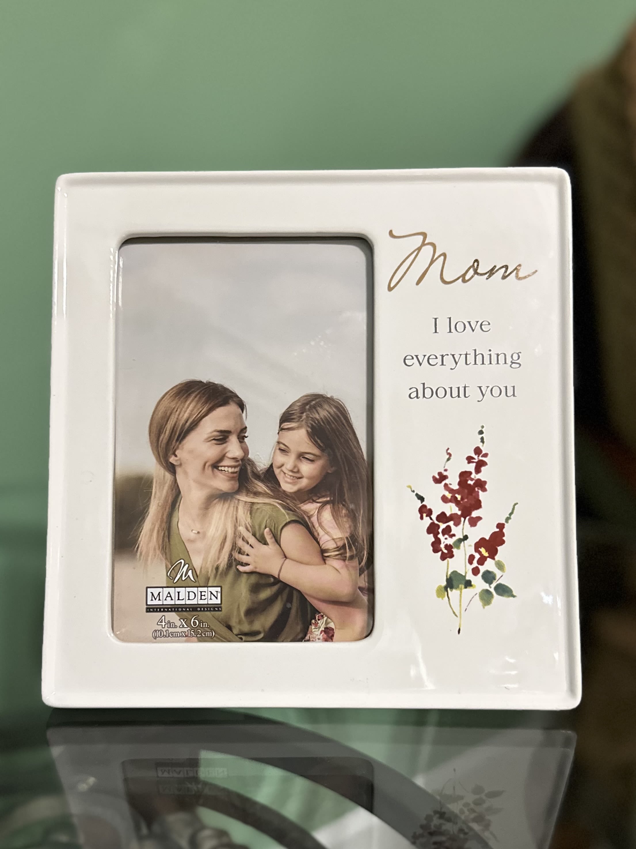 "Mom I Love Everything About You" Picture Frame "Mom I Love Everything About You" Picture Frame - This beautifully glazed ceramic frame features a clean, modern design with soft floral accents and a touching message: "Mom – I love everything about you." The sweet sentiment, paired with a cherished photo, makes this frame the perfect keepsake for Mother's Day, birthdays, or any day you want to remind her how special she is. Its glossy finish and delicate artwork offer a timeless look that will complement any décor, while its heartfelt message adds emotional warmth to any space. Photo size: 4" x 6" (10.1 cm x 15.2 cm)