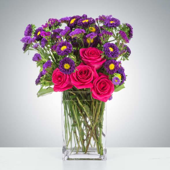 Twilight Glow by BloomNation™ - This pink and purple arrangement is tough! Purple Matsumoto asters, purple statice, and hot pink roses are all sturdy flowers and will provide your recipient with a fresh-looking arrangement for a long time. A good option to send for celebrating a birthday, a graduation or just because.  Approximate Dimensions: 14&quot;D x 18&quot;H