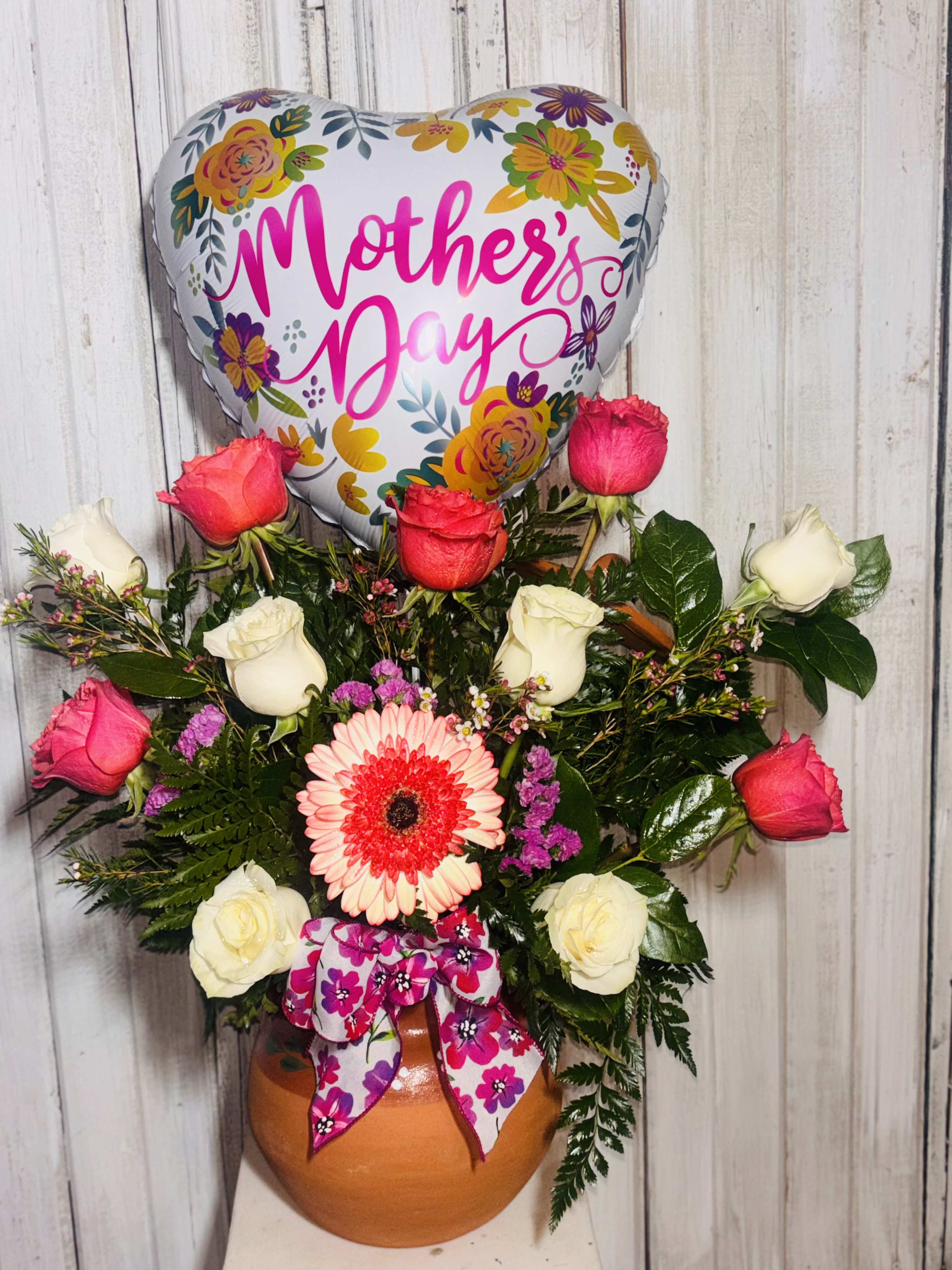 La Grande Mamma La Grande Mamma - This arrangement contains a clay pottery with lid. Roses, greenery and gerber Daisy.