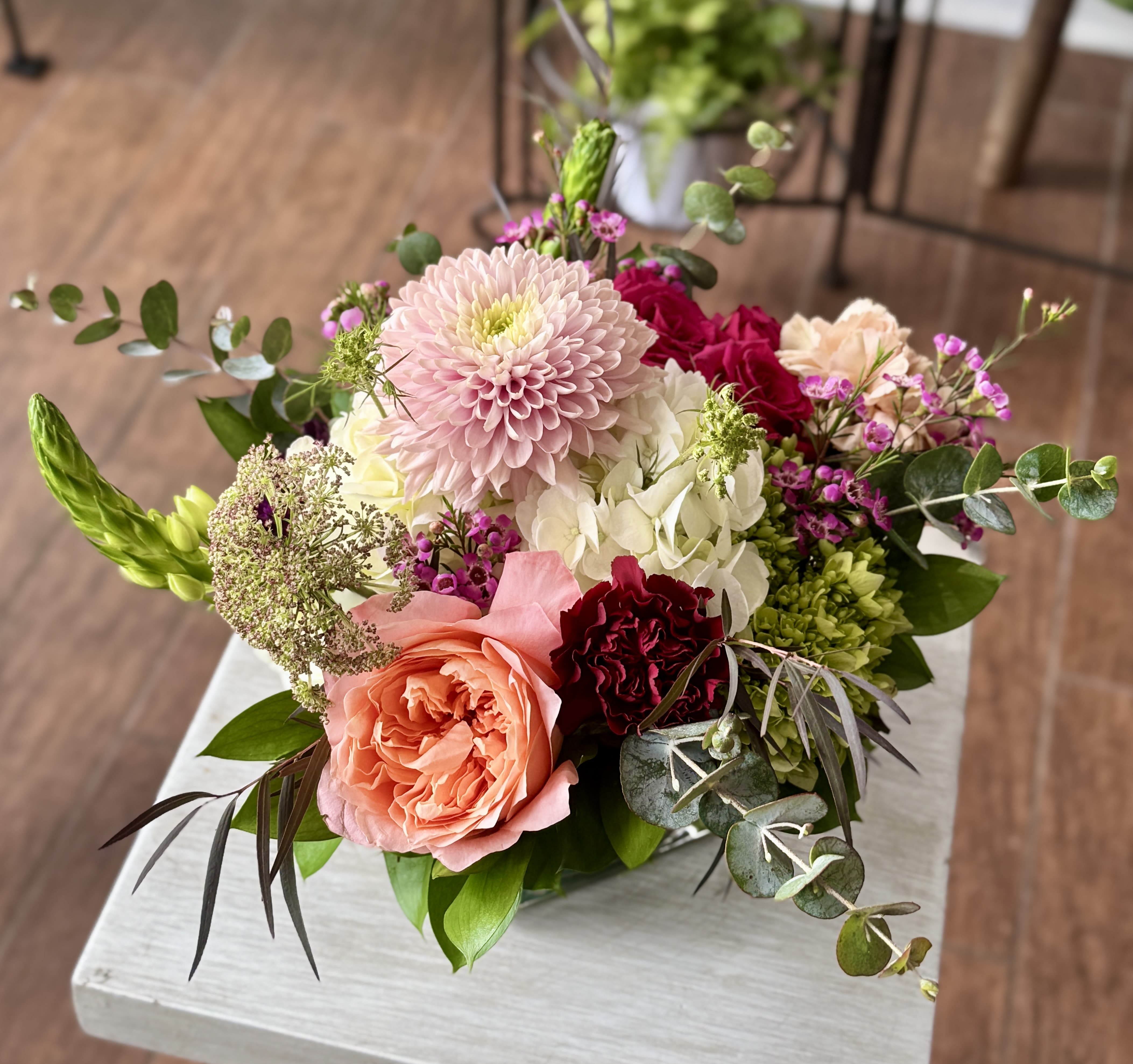 Stacie - A variety of flowers in a short design with seasonal accents, arranged in a clear glass cube vase.
