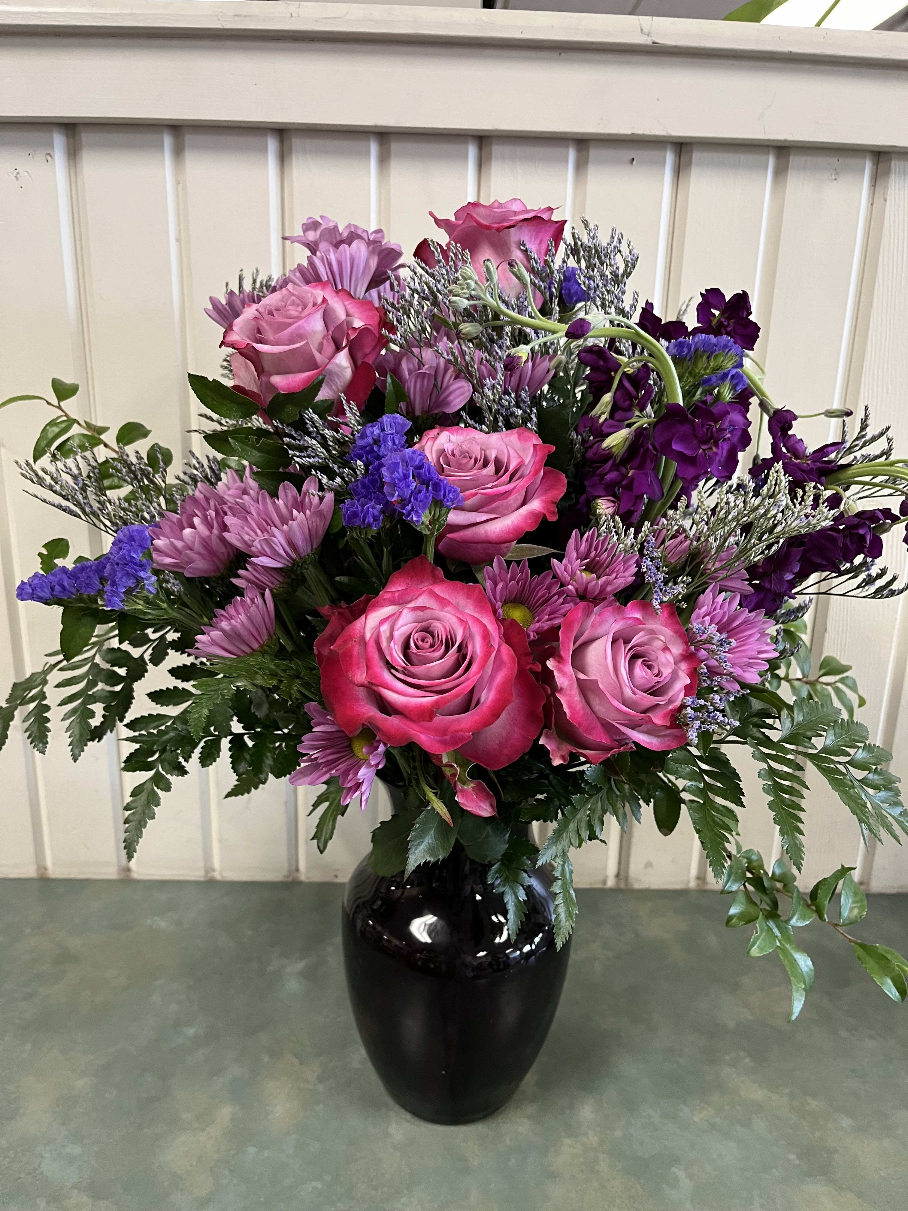 Lavender Wish Bouquet - One sided arrangement with lavender roses, stock, mums and assorted greenery in a purple glass vase.  
