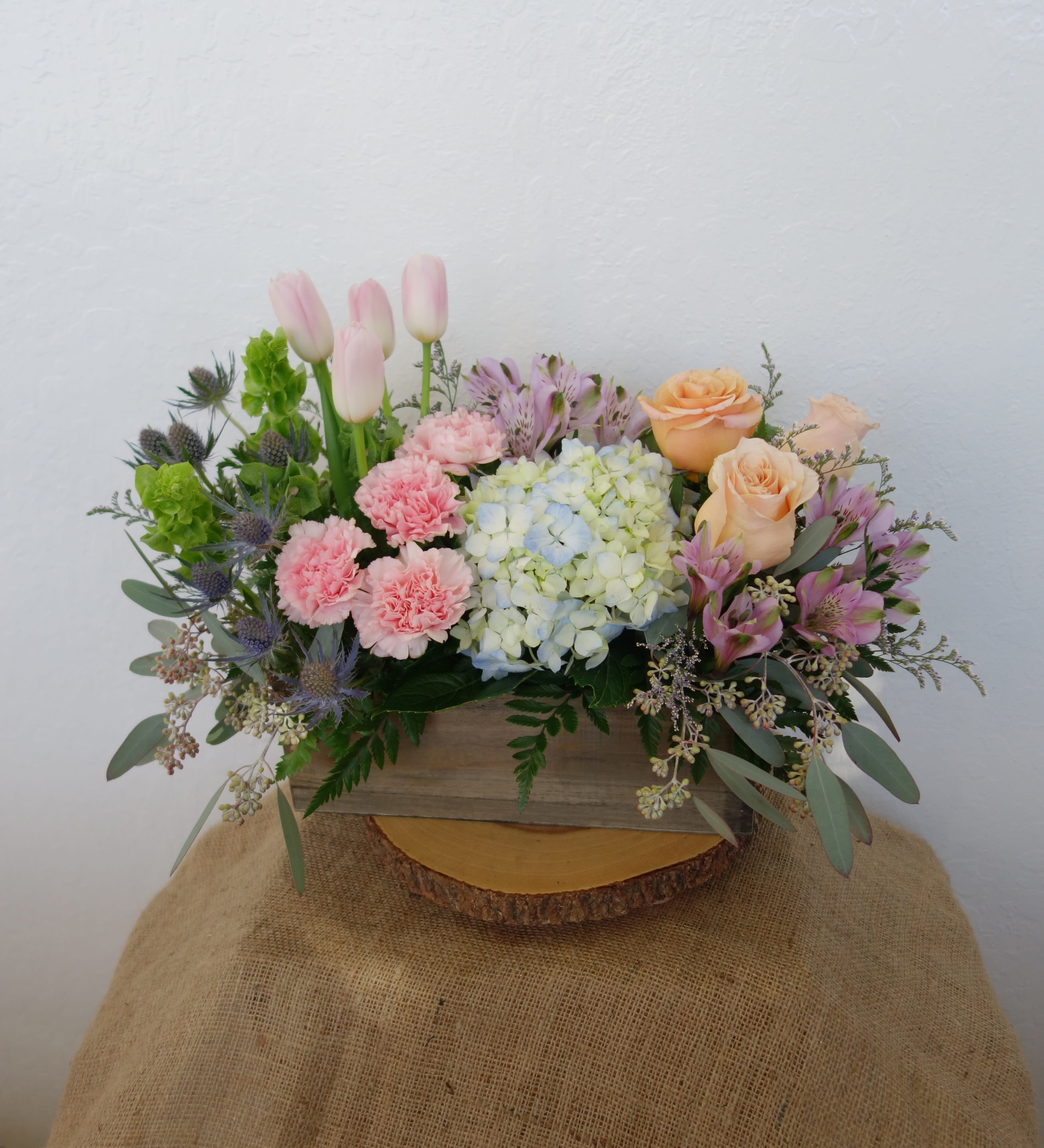 Secret Garden - Pastel Colors Secret Garden - Pastel Colors - A secret garden lies within our imaginations, a sight to behold. This unique pastel-colored arrangement features roses, hydrangeas, tulips, carnations, alstroemerias, sea holly, and mixed foliage. Deluxe (as shown) The arrangement is approximately 14" H and 15" W (Woodbox 12" W)