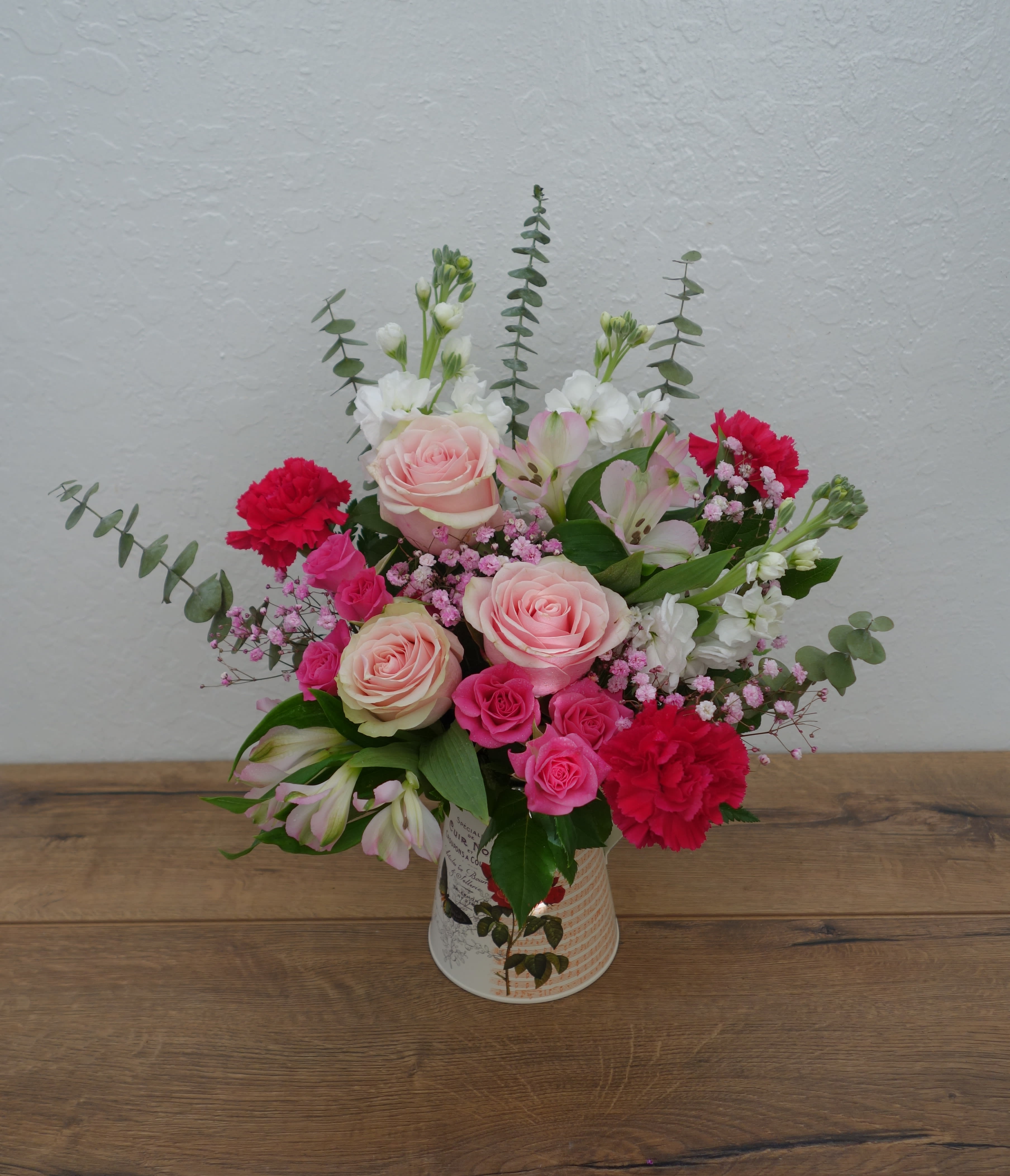 Mother Knows Best - Even if we're all grown up... sometimes our mothers remind us that she still knows best. This pink, hot pink, and white mother's day arrangement features roses, carnations, spray roses, alstroemerias, stocks, baby's breath with mixed foliage in a pitcher.