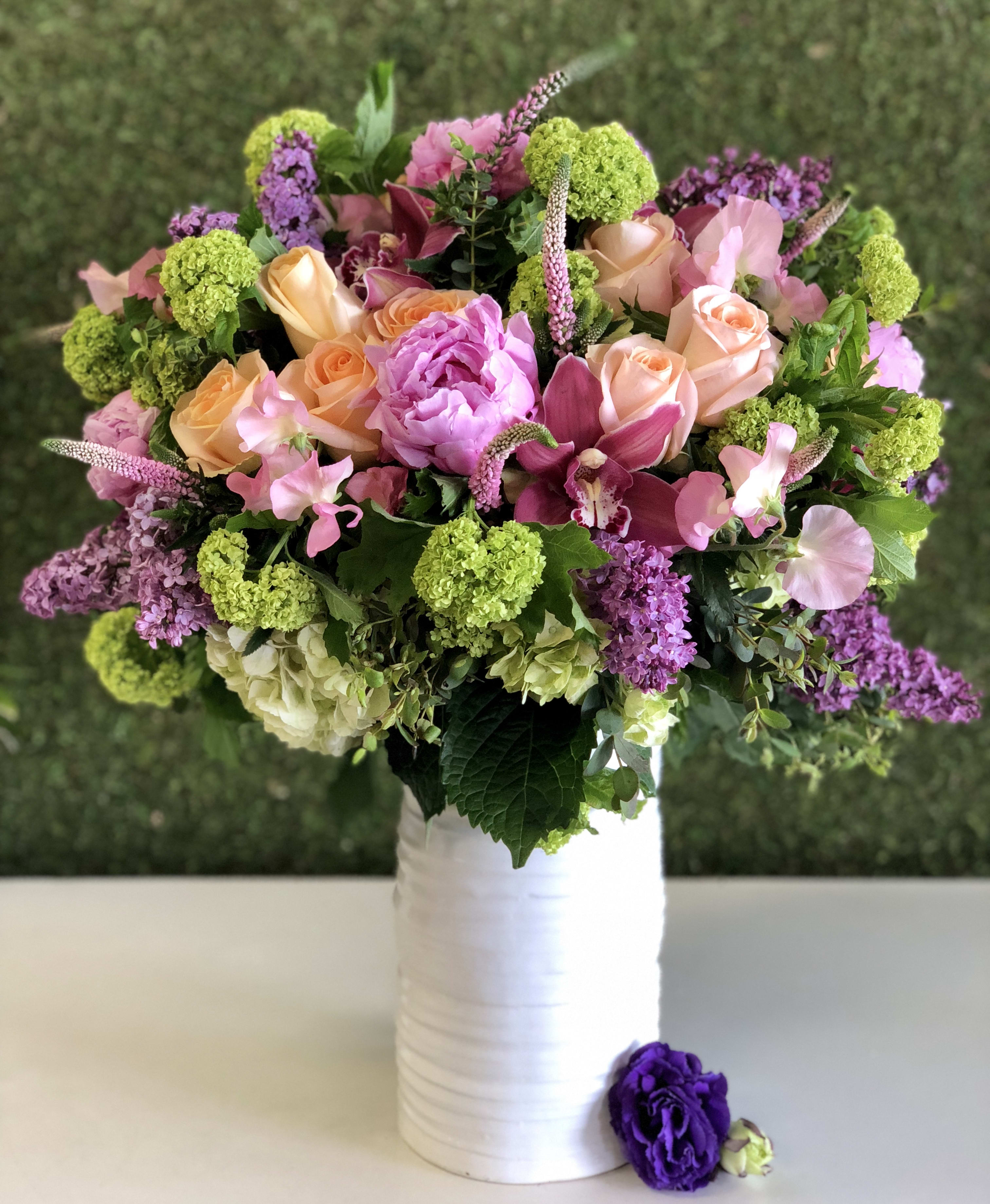 Georgina - Extravagant Design with Peonies, Roses and more - This extravagant bundle is a sure show stopper! (We're speaking from experience). An all around design full of peach roses, peonies, orchids, hydrangeas, lilacs, and timeless blooms all on a white ceramic vase. 