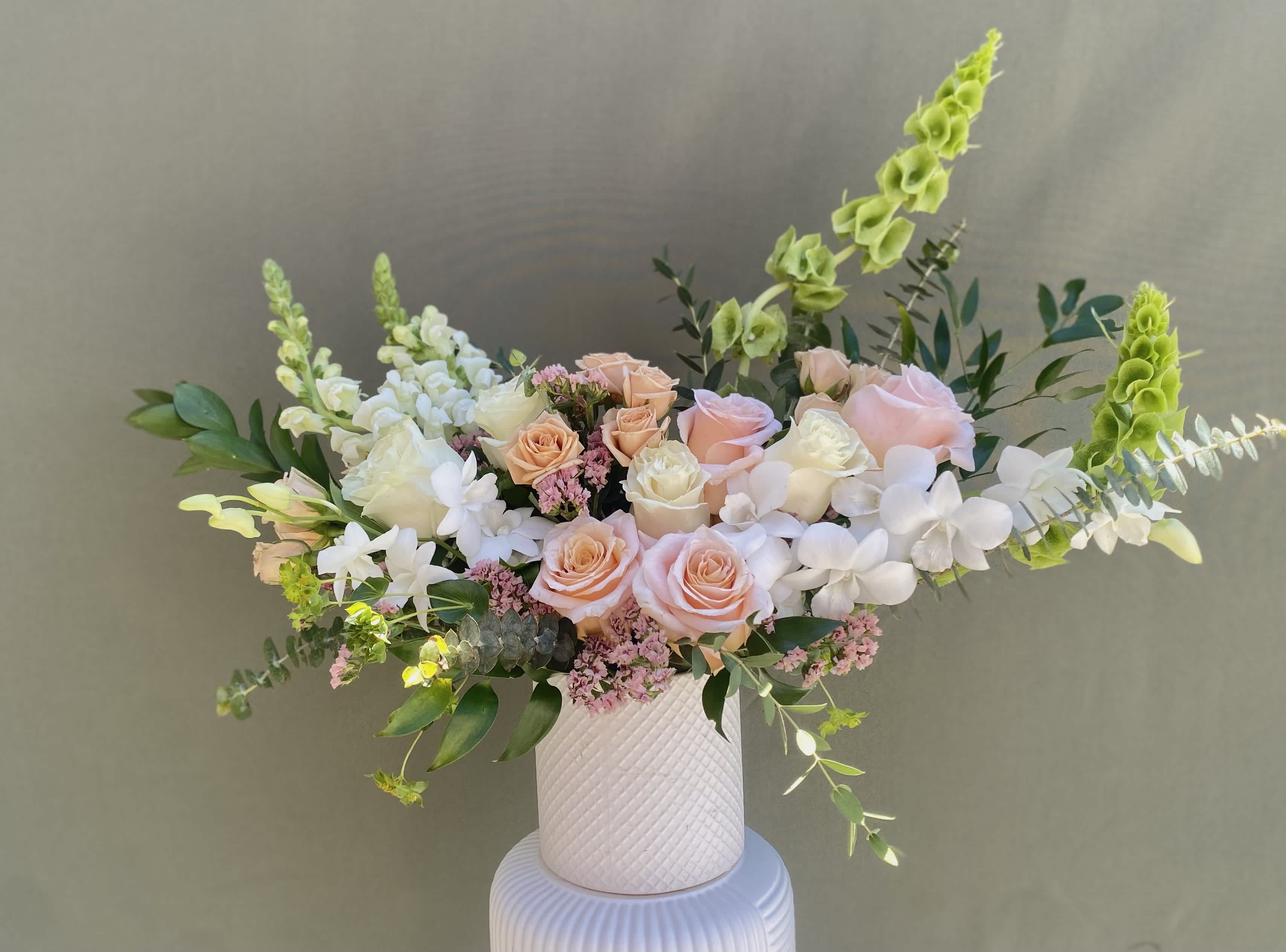 Venice Peach - Whimsical and romantic, this arrangement has some seriously sweet vibes. Soft peach and white roses, spray roses, snapdragons, and Bells of Ireland are complemented with white dendrobium orchids and eucalyptus