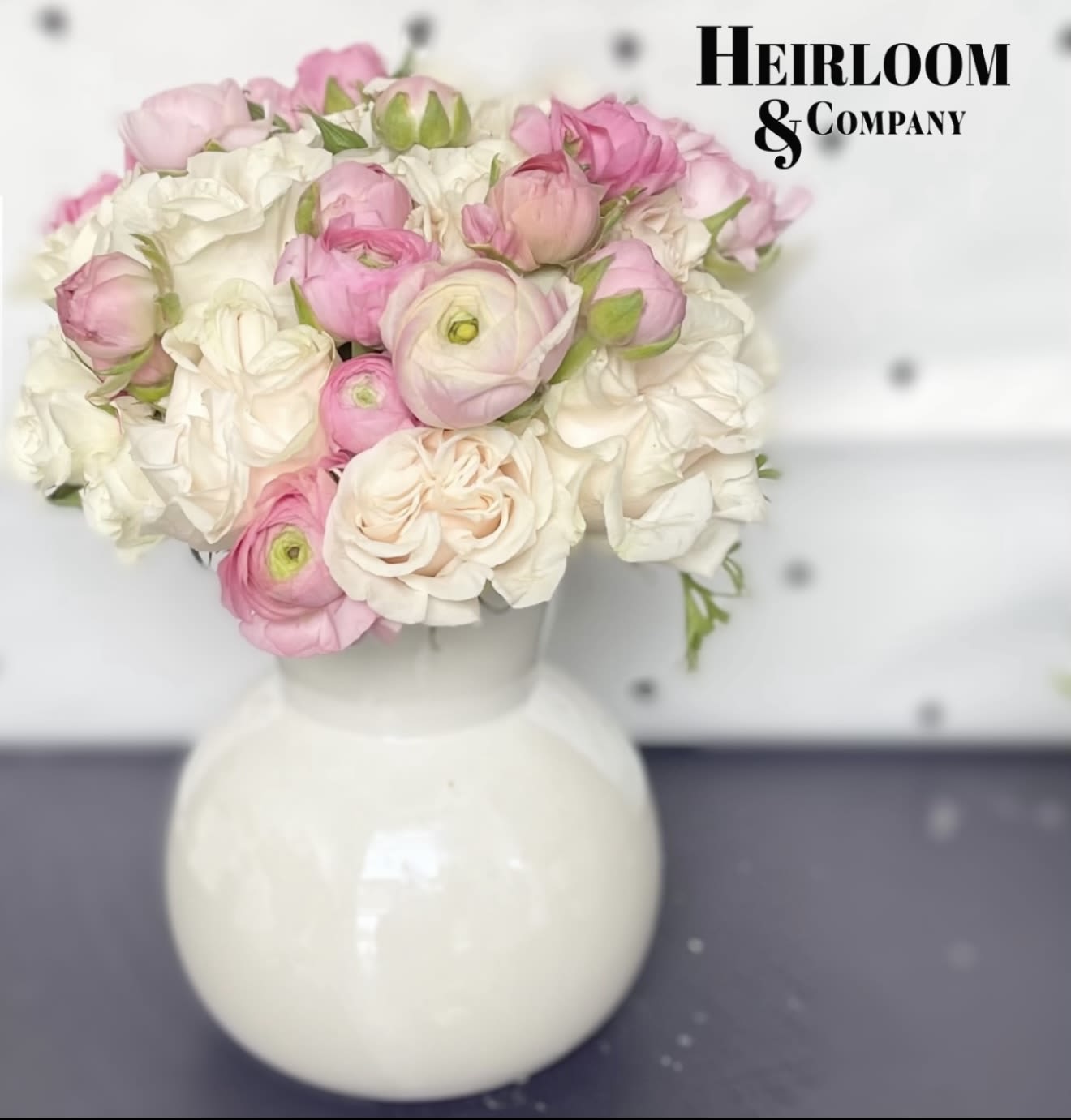 Taylor’s Garden Rose Arrangement  - An elegant blend of soft blush ranunculus, ivory garden roses, and ruffled petals arranged in a round white vase. With its romantic color palette and full blooms, this design is made for weddings, baby showers, or heartfelt moments.
