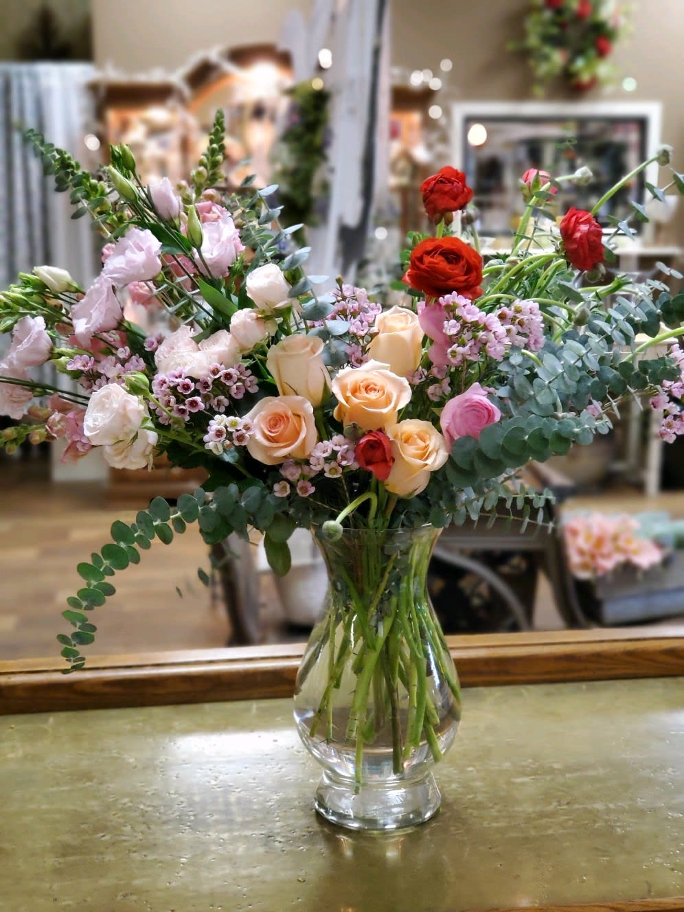 Pop Of Red Pop Of Red - Roses, ranunculus, spray roses, lisianthus, snapdragons and eucalyptus in a tall clear glass vase