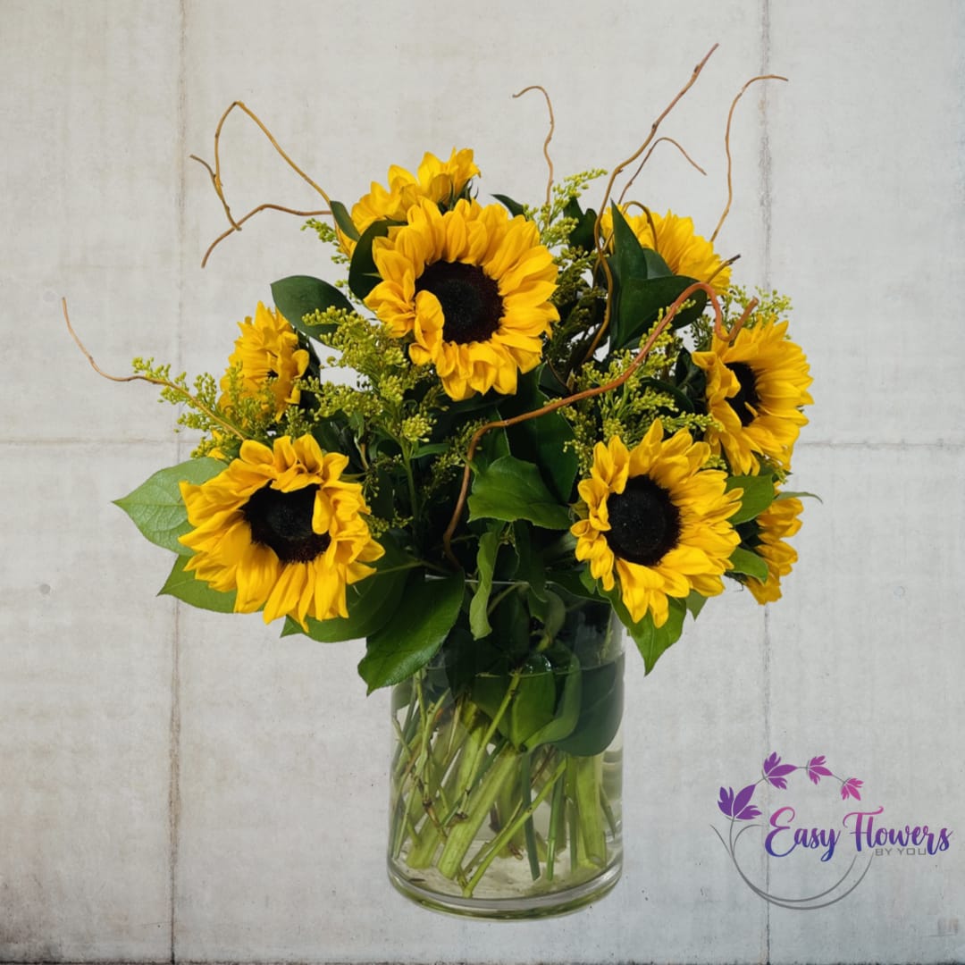 Sunny Sunflowers - &quot;Brighten Your Day with Our Springtime Smiling Sunflowers - Looking for a simple yet exquisite arrangement that will bring a touch of sunshine to your home or office? Our stunning bouquet features vibrant sunflowers and coordinating foliage, expertly arranged in a clear glass vase. Perfect for any occasion, this delightful arrangement is sure to put a smile on your face and brighten up any room.