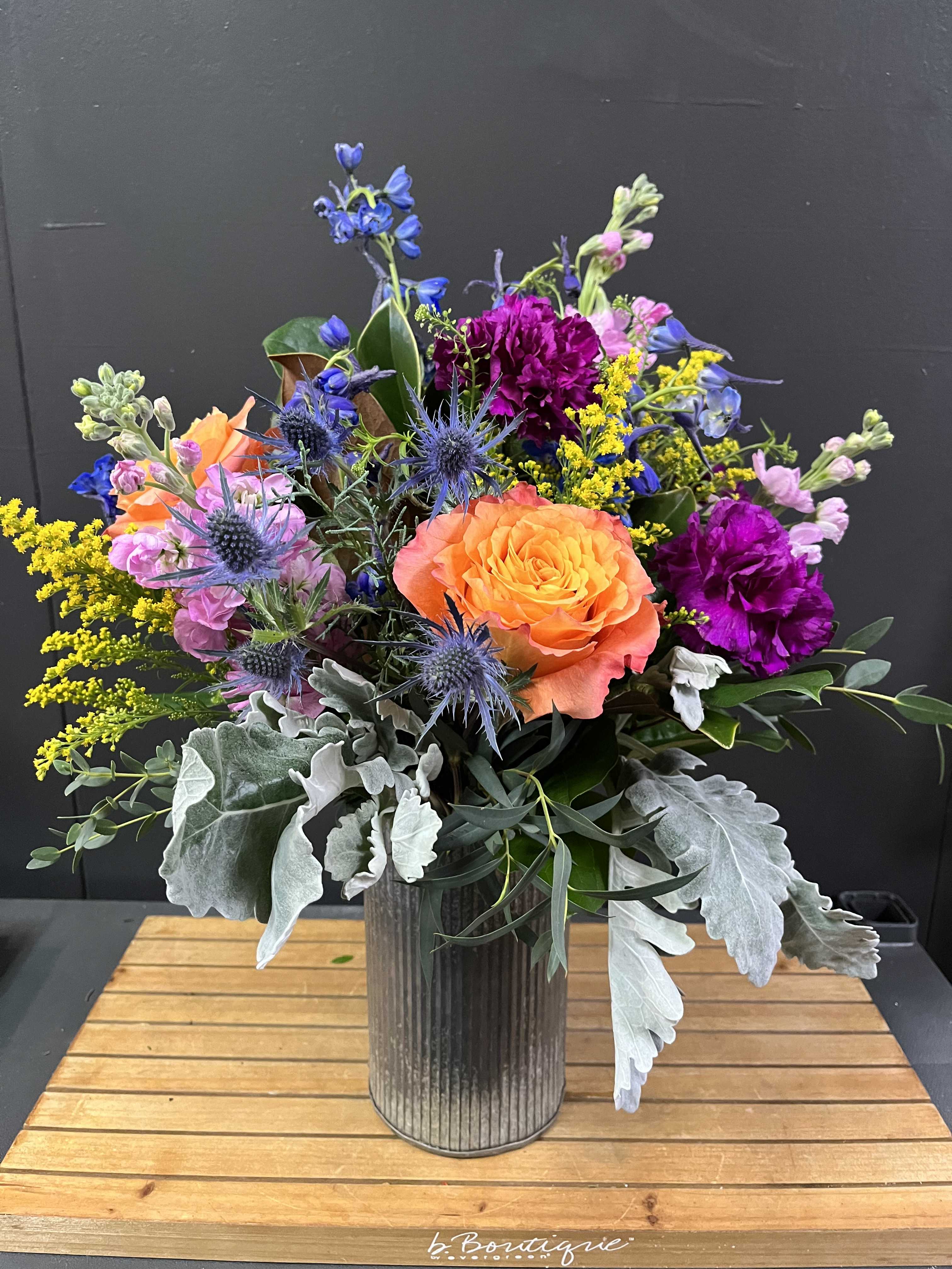 Rustic Garden - This rustic colorful bouquet is one sided and in a tin container.  *Some stages of flower life may vary. (Example: Lilies may be more open than imaged.)  Flower shortages and product availability means that some substitutions will apply. Value will always be filled.  This bouquet might include eucalyptus amongst the greenery. It may be toxic to pets including but not limited to Cats and Dogs if digested