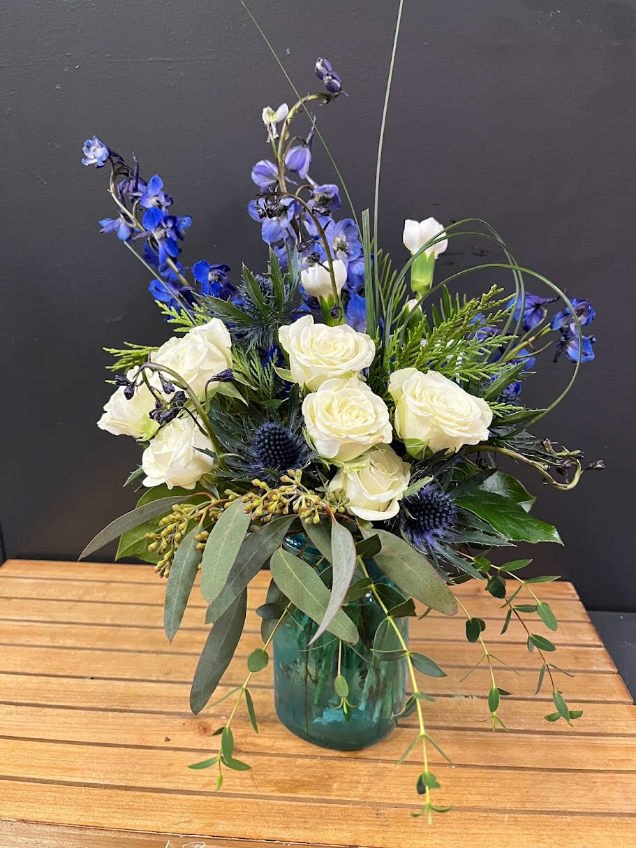 Simple Jar of Blue - An all around flower arrangement designed with fresh flowers to include white spray roses, blue delphinium and lots of beautiful greens.  * Some stages of flower life may vary. (Example: Lilies may be more open than imaged.)  Flower shortages and product availability means that some substitutions will apply. Value will always be filled. This bouquet might include eucalyptus amongst the greenery. It may be toxic to pets including but not limited to Cats and Dogs if digested.