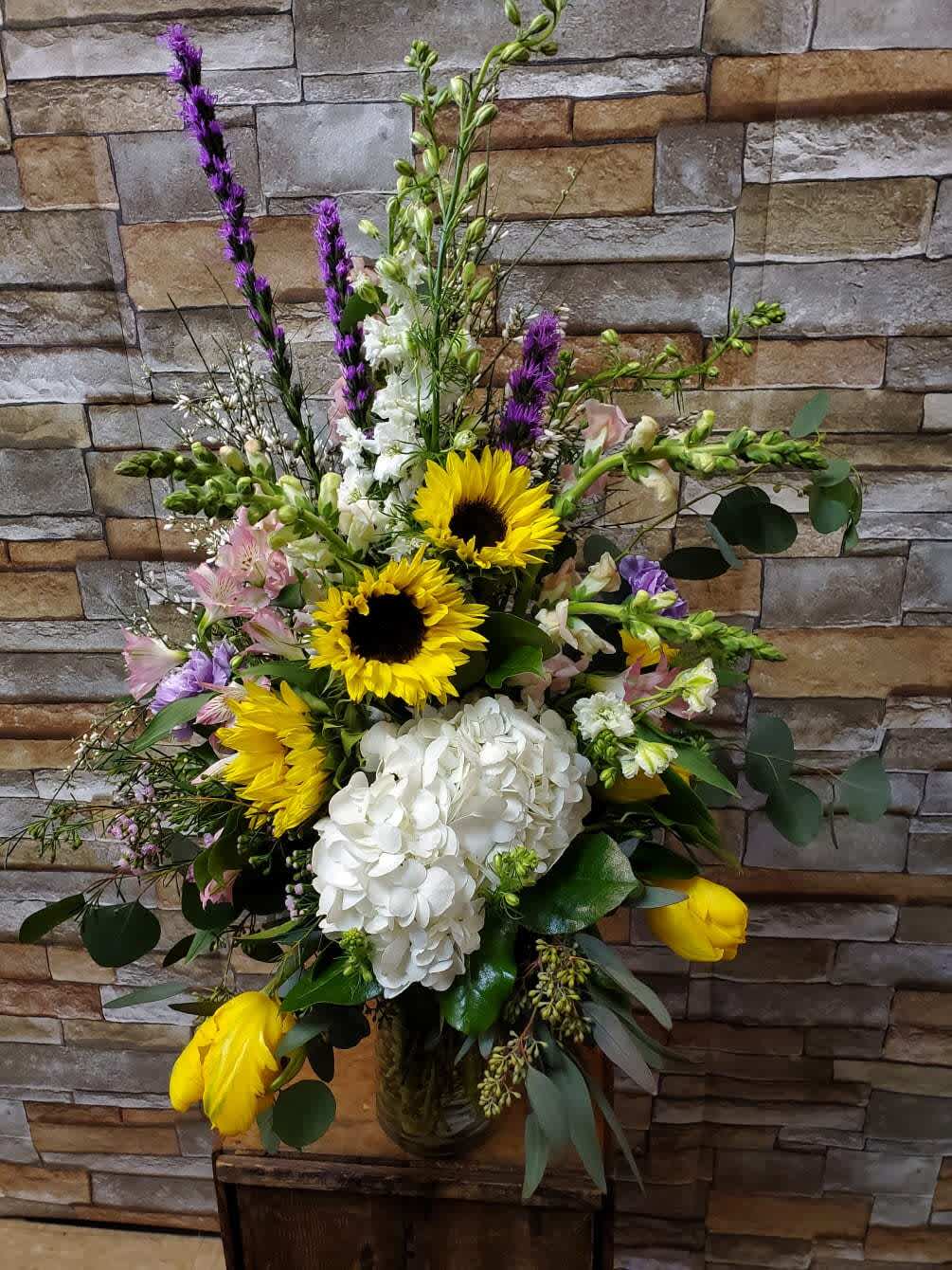 Spring Garden - A beautiful one sided arrangement. Made with fresh flowers to include, alstromeria, sunflowers, larkspur, liatris, tulips, hydrangea, snapdragons and filler flowers.  * Some stages of flower life may vary. (Example: Lilies may be more open than imaged.)  Flower shortages and product availability means that some substitutions will apply. Value will always be filled.  This bouquet might include eucalyptus amongst the greenery. It may be toxic to pets including but not limited to Cats and Dogs if digested.