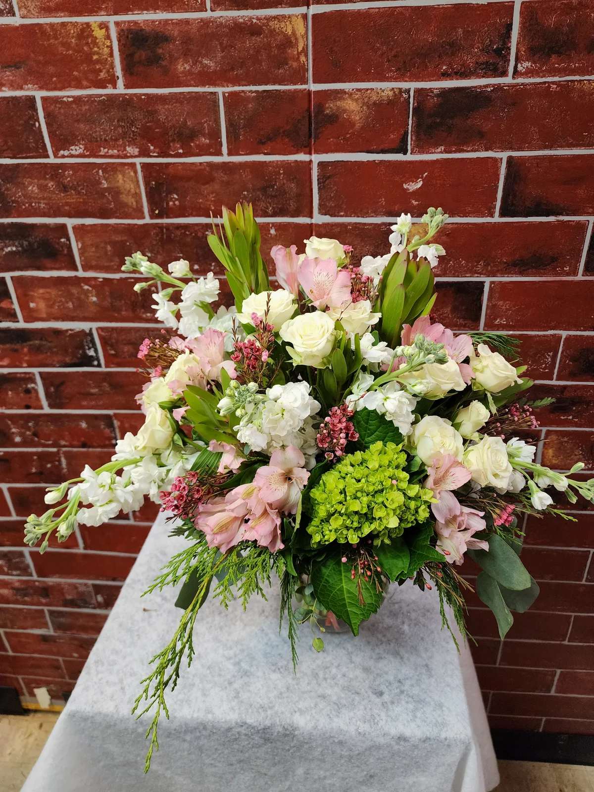 Elegantly Petite - Designed with fresh flowers. This product is one sided design.  * Some stages of flower life may vary. (Example: Lilies may be more open than imaged.)  Flower shortages and product availability means that some substitutions will apply. Value will always be filled.  This bouquet might include eucalyptus amongst the greenery. It may be toxic to pets including but not limited to Cats and Dogs if digested.