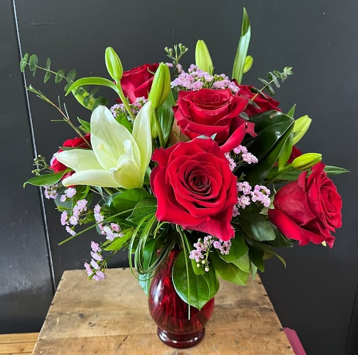 Playful Red Roses and Lilies. - This bouquet is designed all around with red roses, white lilies, pinkish/lavender wax flower. Designed with a nice mix of greenery for lots of fun texture.  *Some stages of flower life may vary. (Example: Lilies may be more open than imaged.)  Flower shortages and product availability means that some substitutions will apply. Value will always be filled. This bouquet might include eucalyptus amongst the greenery. It may be toxic to pets including but not limited to Cats and Dogs if digested.