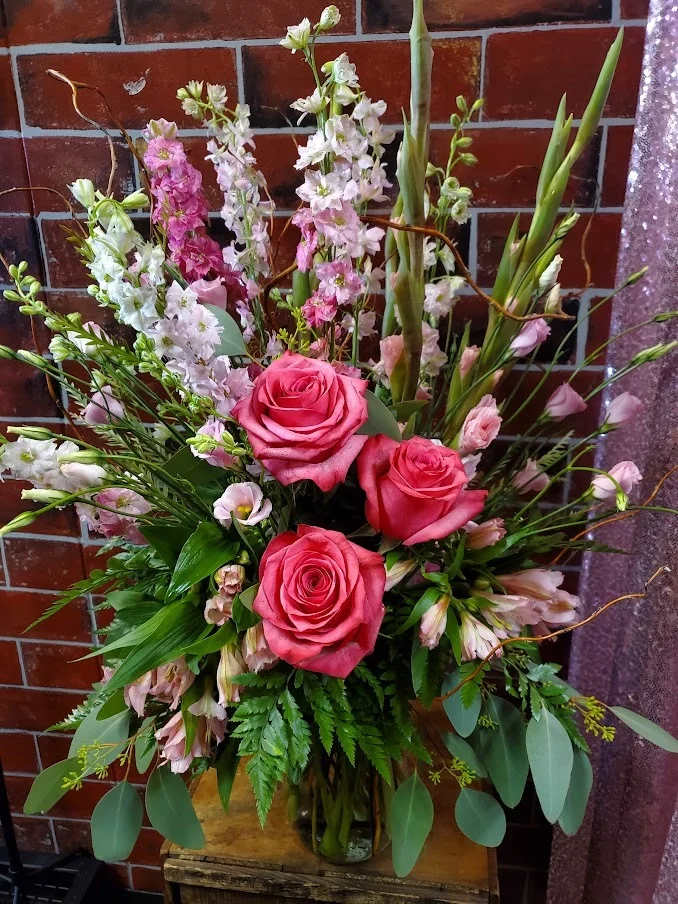 Pretty In Pink - Designed one sided with fresh flowers to include Pink Roses, Pink Larkspur, Pink Gladiolous Pink Alstromeria and Pink lisianthus  * Some stages of flower life may vary. (Example: Lilies may be more open than imaged.)  Flower shortages and product availability means that some substitutions will apply. Value will always be filled.  This bouquet might include eucalyptus amongst the greenery. It may be toxic to pets including but not limited to Cats and Dogs if digested.