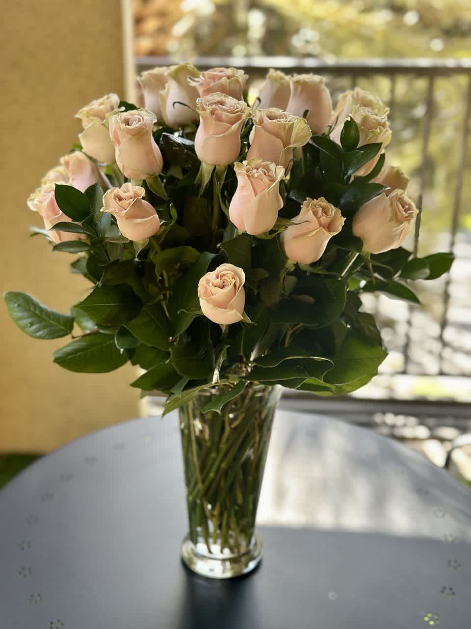 2 Dozen Light Pink Roses - A joyful gesture of love and affection, this chic arrangement of light pink roses with fresh greens is a special surprise on any occasion. The light pink roses are arranged with salal and delivered in a clear vase.