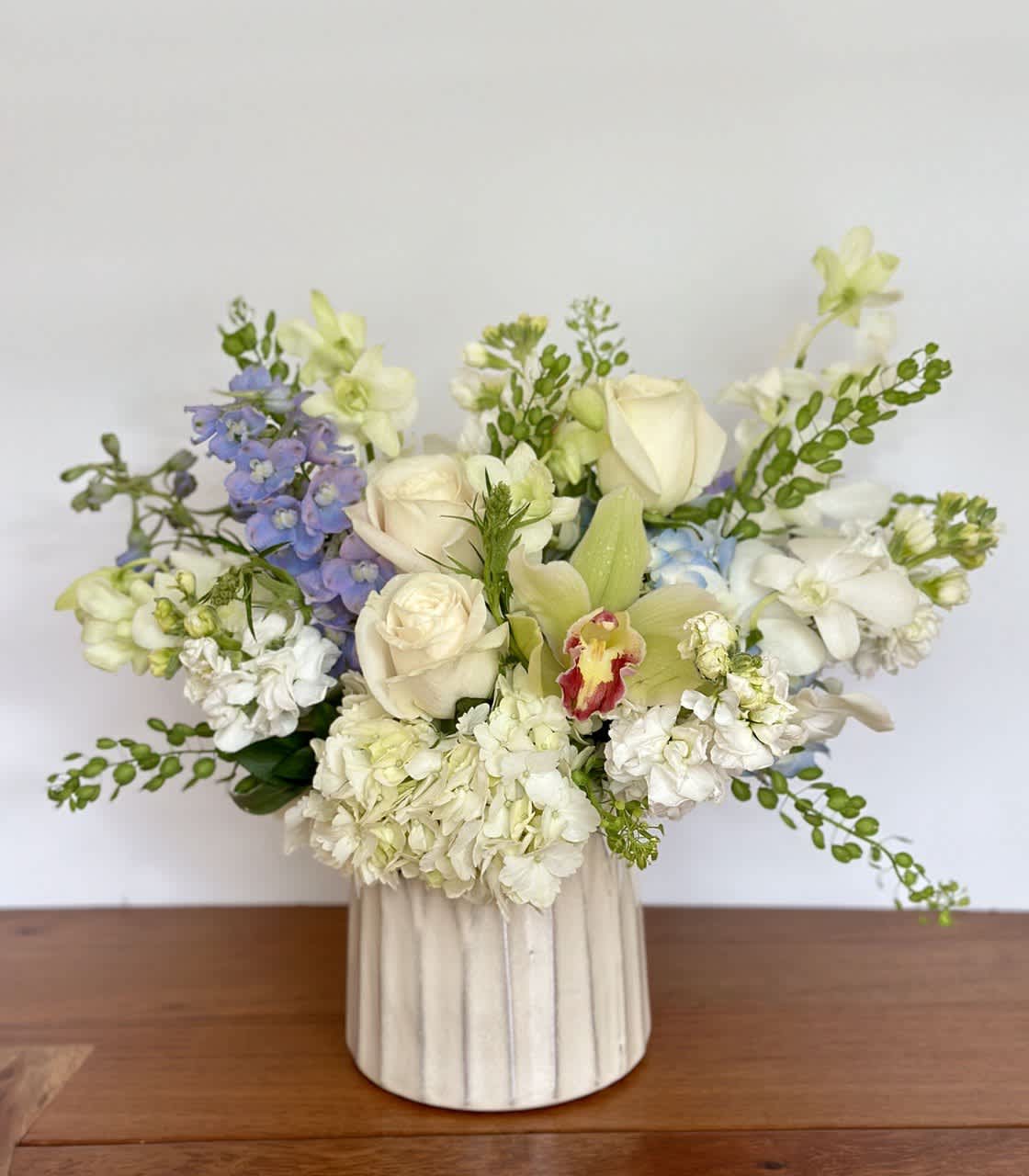 Pearl - This beautiful arrangement of flowers in a ceramic vase features a mix of white, blue, and green blooms. It's the perfect gift to bring a smile to someone's face.