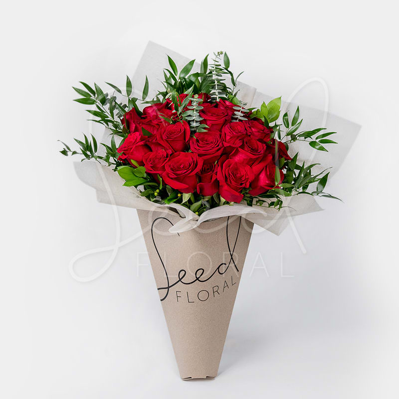 24 Carat Rose Bouquet - Timeless. Classic. Romantic. Hand wrapped bouquet featuring 2 dozen long stem premium Red Roses framed with lush and glossy foliage. Hydration packet included
