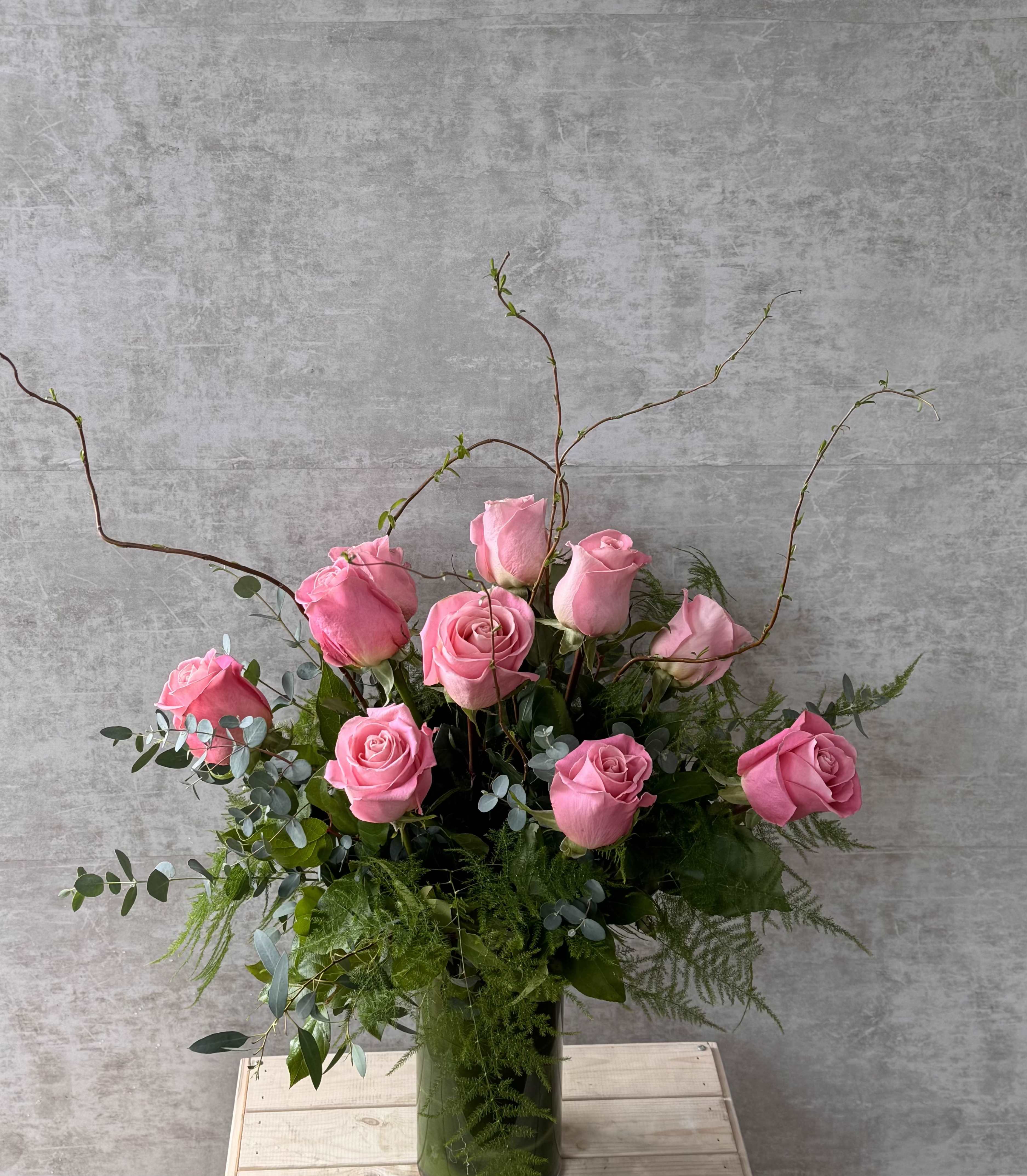 One Dozen Pink Roses - A graceful arrangement of one dozen pink roses, beautifully mingled with delicate lilac blooms and fresh eucalyptus. This enchanting bouquet, presented in a modern leaf lined vase, is a poetic expression of love and appreciation, perfect for Mother's Day, birthdays, or as a heartfelt gesture of thanks.