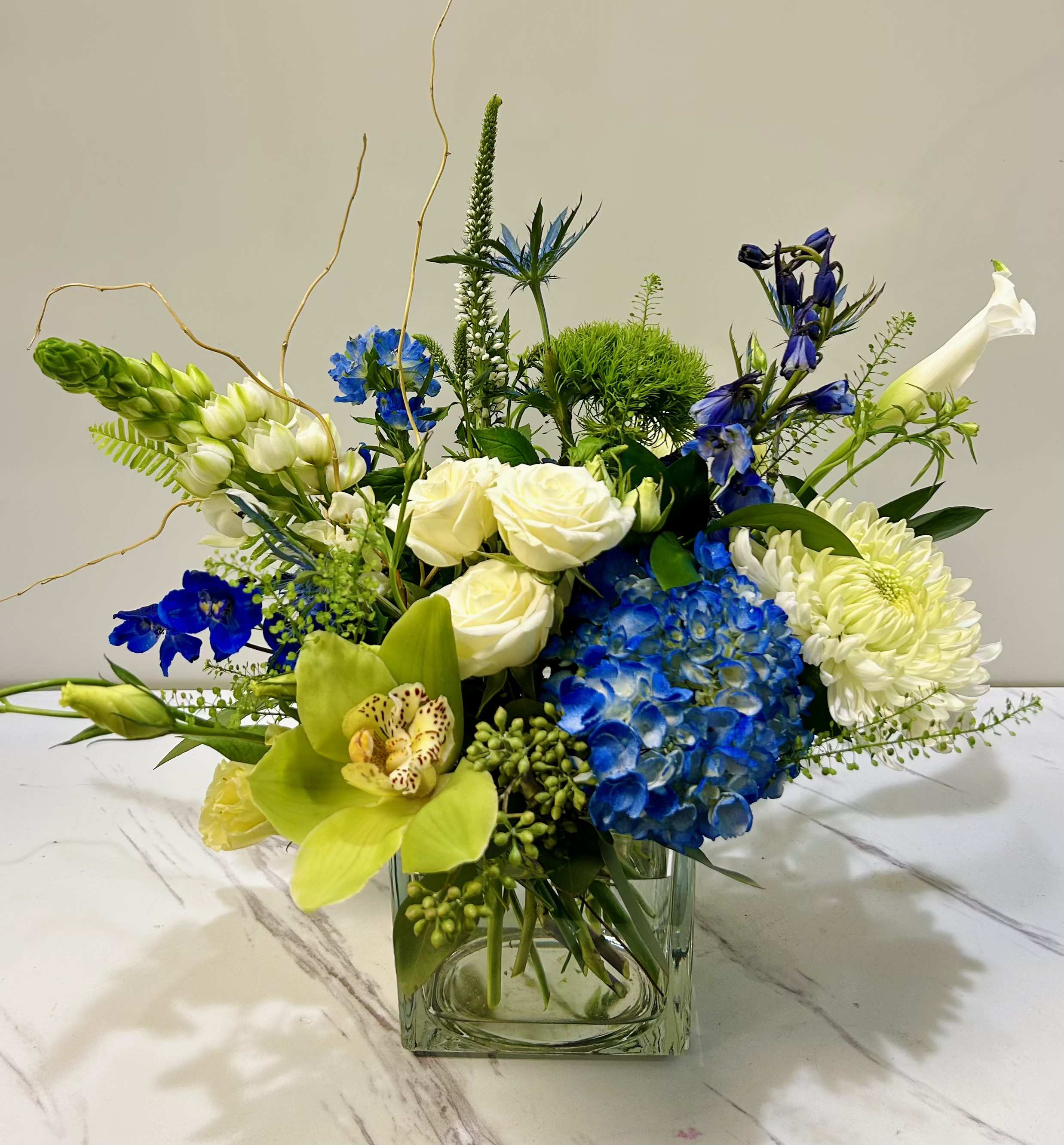 Blue Me Away  - Blue Me Away is a petite  modern and sophisticated arrangement of white and blue blooms, elevated by the elegance of a single white orchid, creating a stunning and contemporary focal point.