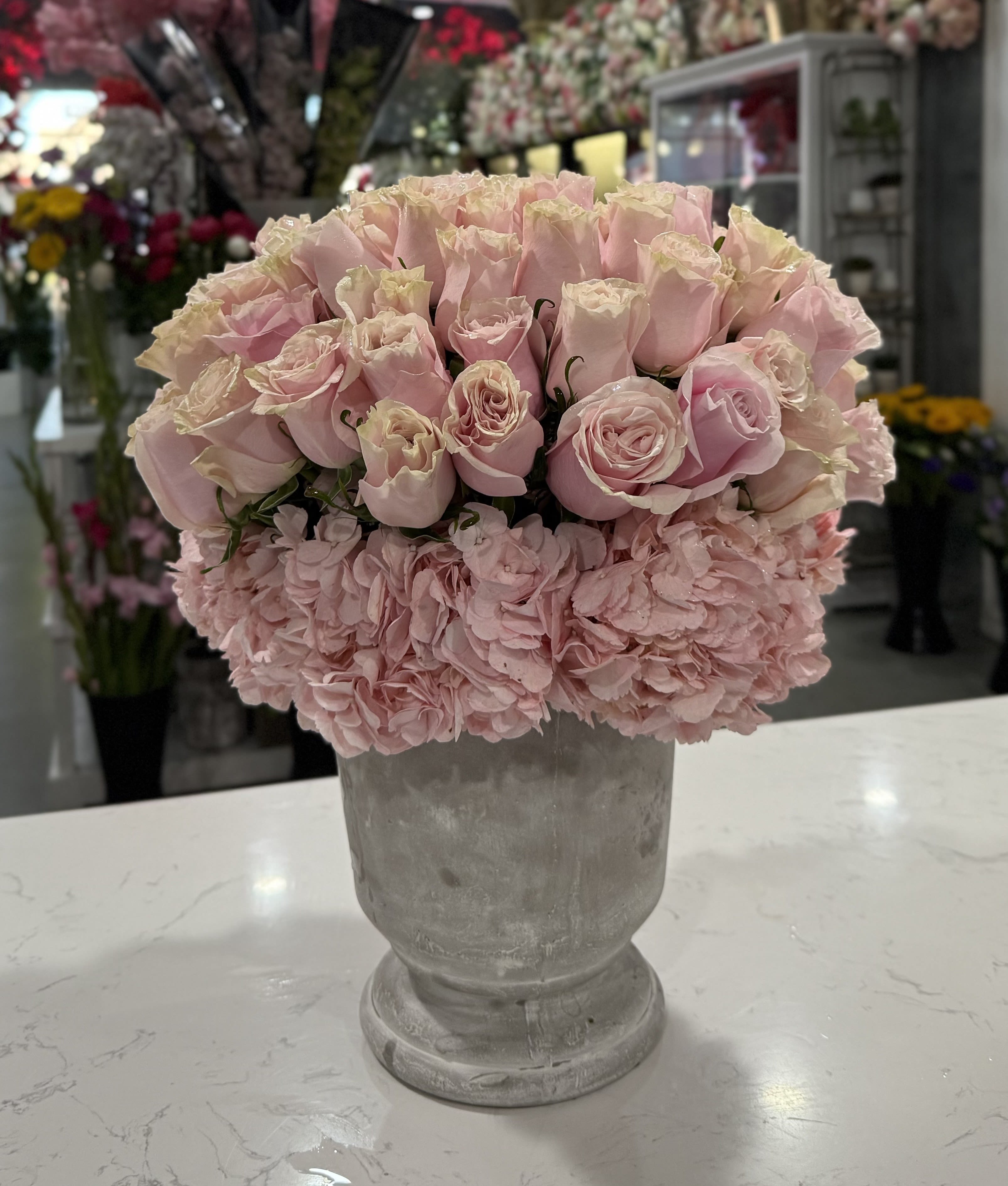 Rose Éclat - An elegant blend of soft pink roses nestled above delicate pink hydrangeas, arranged in a classic stone-textured vase. This design captures timeless romance and gentle sophistication — perfect for expressing love, grace, or appreciation.