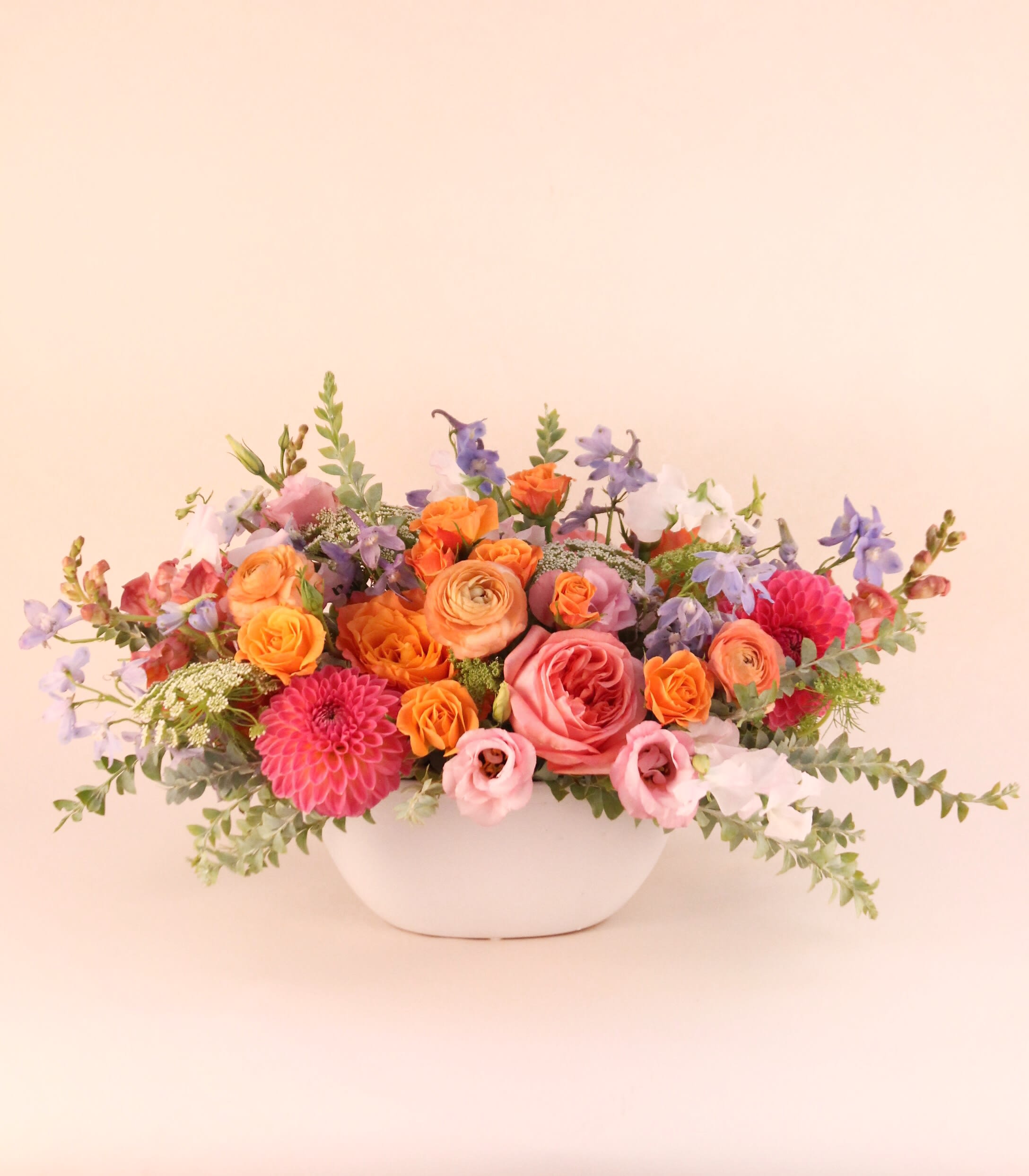 Summer Sensation - Bright and punchy pinks, coral and oranges with a hint of blues come together in a white ceramic vase. Flowers may include dahlias, ranunculus, roses, sweet pea, lisianthus, delphinium, snapdragon, and spray roses.  Vase dimension: 4 H&quot; x 9&quot; L This arrangement is approximately: 10” H x 20” W