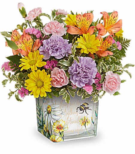 Teleflora's Floral Buzz Bouquet - Like a bee dancing through a hidden garden, this enchanting bouquet of orange, lavender, and yellow blooms in a vintage-inspired glass cube makes for a truly magical gift.