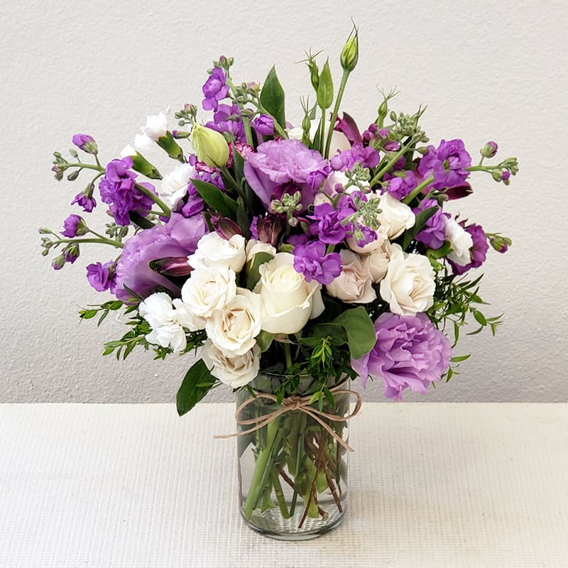 Lavender Fields  - A beautiful blend of white and lavender seasonal flowers accented with lush greens, this bouquet is a true masterpiece.   Expertly arranged by our flower stylists and finished with a touch of love in a sleek cylindrical glass vase, it’s the perfect gift to express admiration, celebrate special moments, or simply add floral elegance to any space.  Approximate Size: 16&quot; H x 15&quot; W. Order now to send a splash of lavender beauty! 