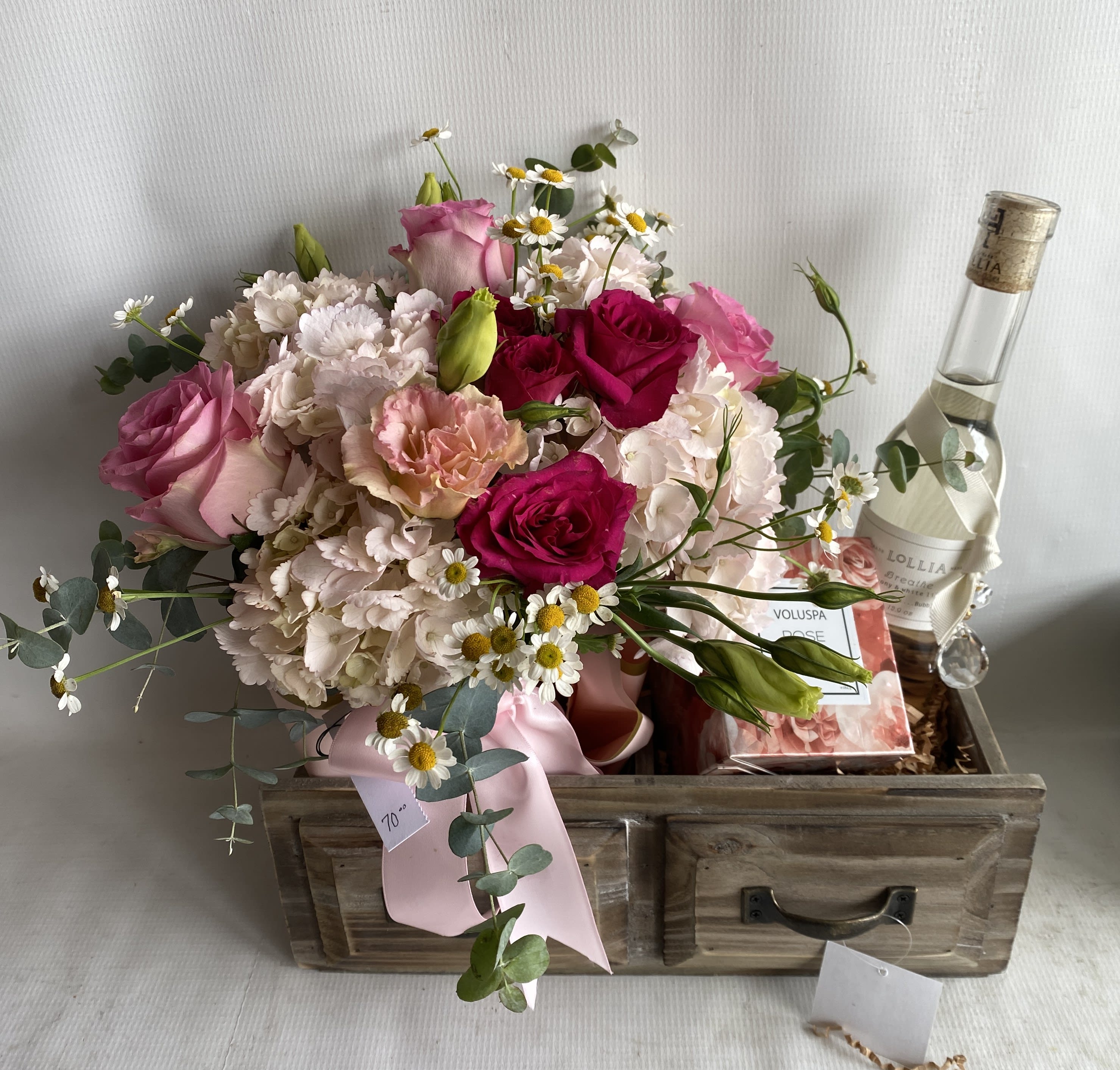 Pampering - Indulge your senses with this rustic wooden box filled with delightful fragrances and seasonal flowers. Along with the stunning arrangement of blooms, this gift also includes a 12 oz Lollia bath soap bottle and an 11 oz Voluspa candle in the enchanting Rose Otto scent. The box measures 12 inches by 6 inches and is perfect for a luxurious and relaxing experience.