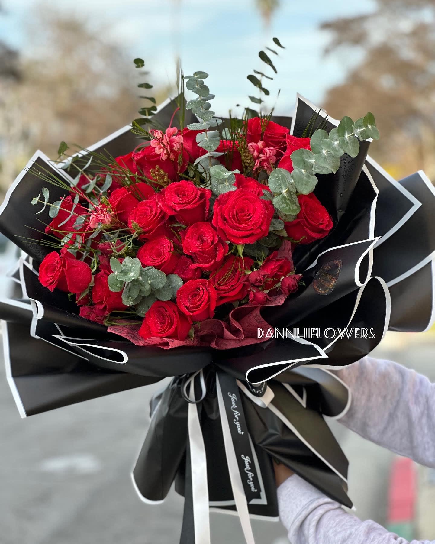 Bouquet 01 - A mix bouquet of red roses, spray roses and season red blooms, wrapped in deluxe black paper wrap. Photo is DELUXE size. STANDARD will be slightly smaller.  Every arrangement is one of a kind and styled with your color selection and desired size in mind. Because we always use the freshest blooms we can get our hands on, your final arrangement may not look exactly as pictured due to seasonal availability.