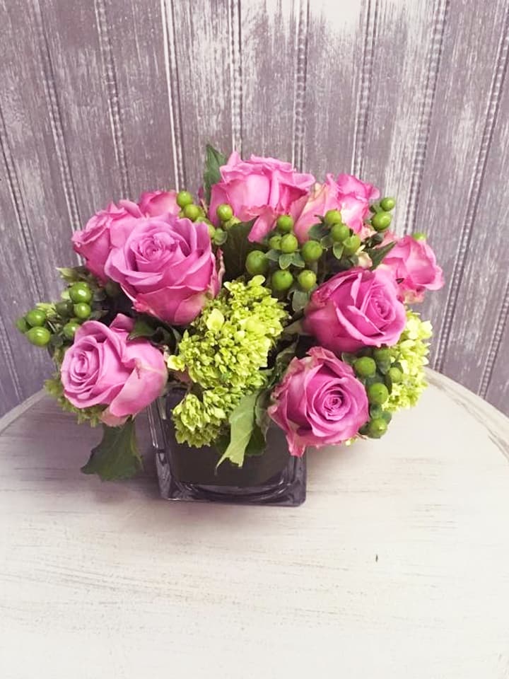Lavender Love - Simple cube vase of purple roses, mini green hydrangeas and hypericum, perfect for a table centerpiece (multiple) or on an end table or coffee table. (image subject to substitutions depending on availability; color scheme and over all feel of arrangement is similar as possible)