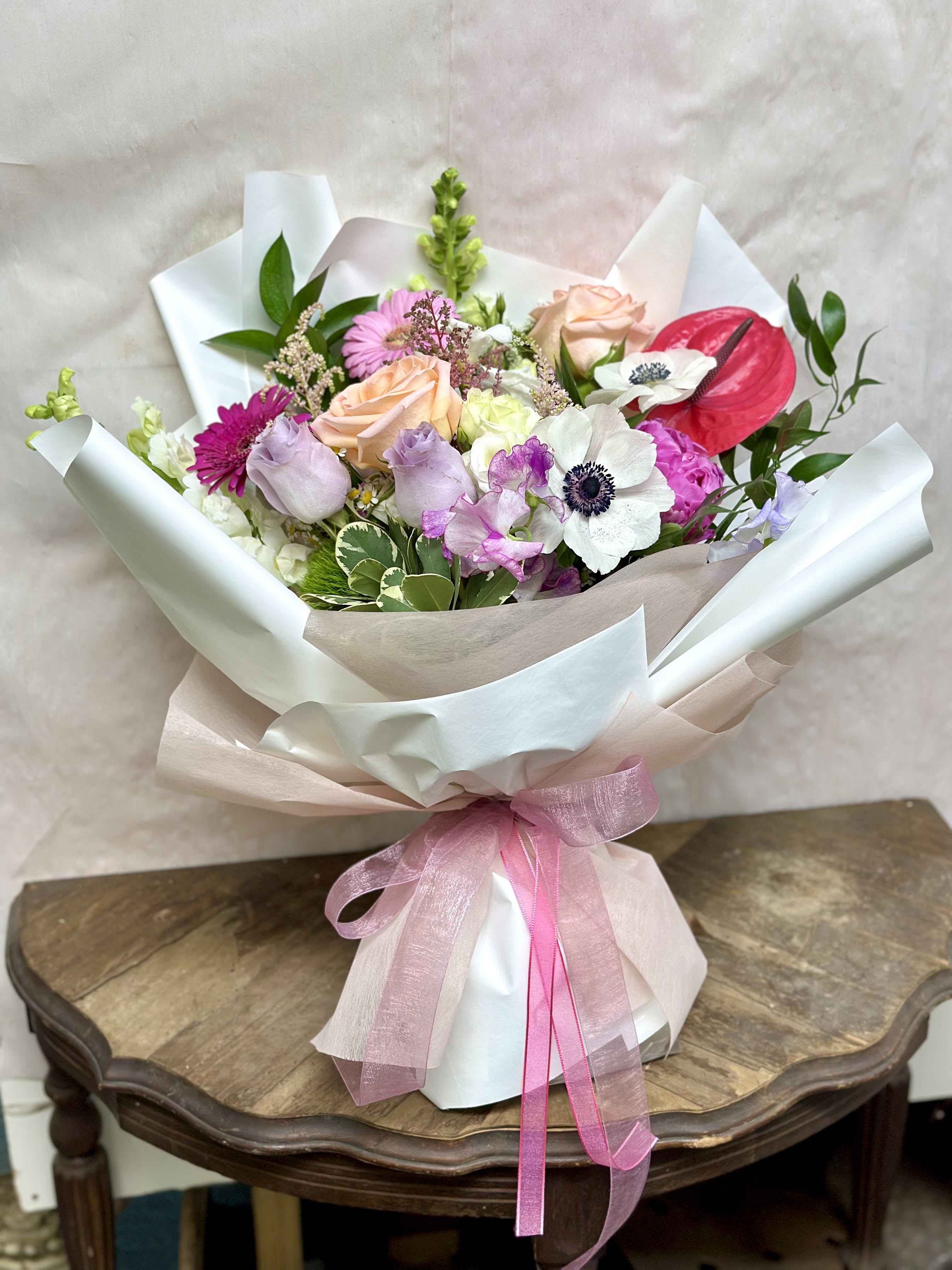 The Queen White & Pink Bouquet The Queen White & Pink Bouquet - This elegant and luxurious bouquet is made up of roses, anemones, snapdragons, ruscus, carnations, and wildflowers. It's large in size due to its rich composition, and the simple wrapping makes the flowers stand out even more. It makes a great gift for anniversaries, birthdays, and more.