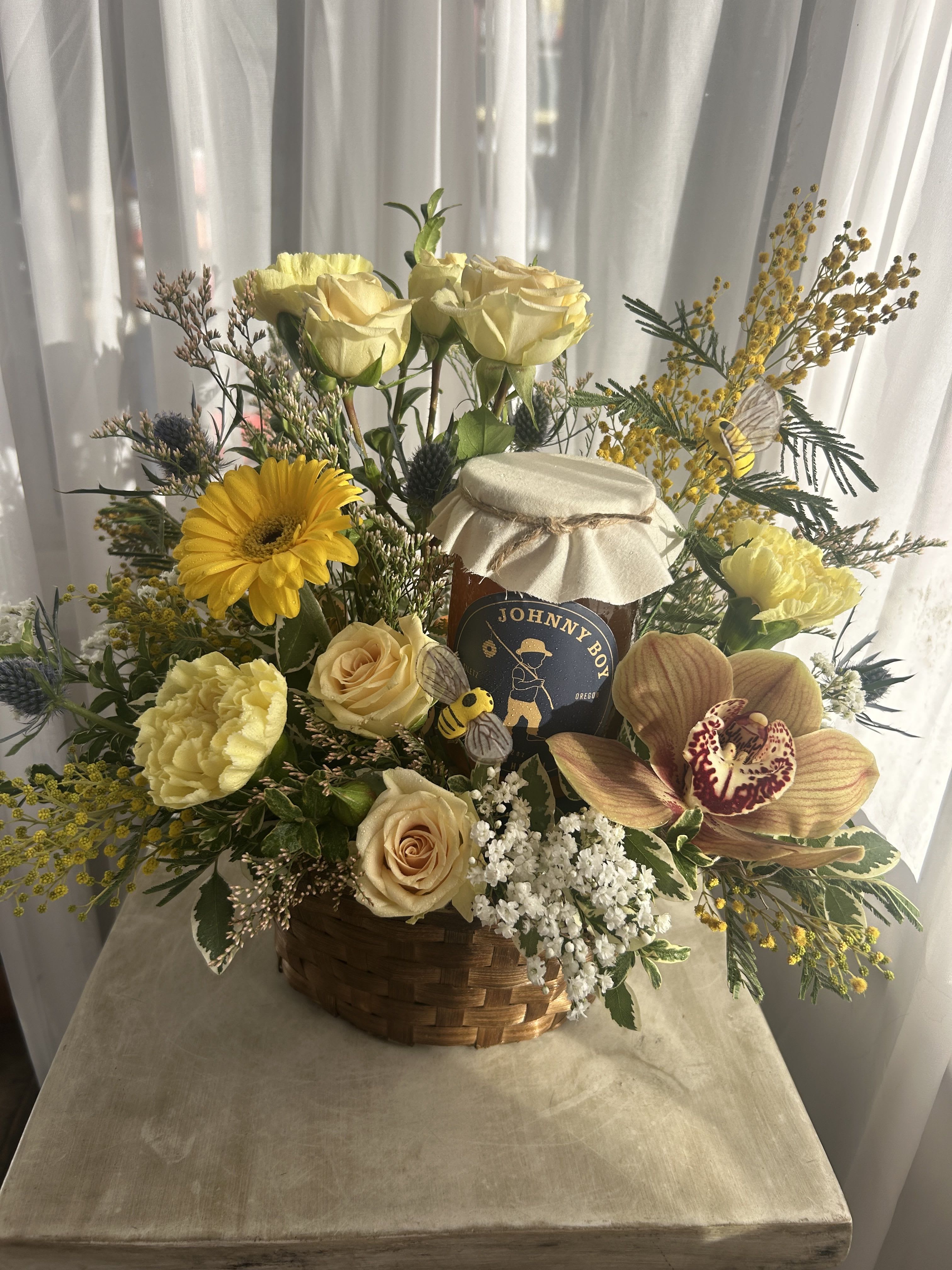 Honey, will you Bee mine? Honey, will you Bee mine? - Honey and flowers...a sweet combination. Carefully collected local wildflower honey bottled by John Smith. Pretty blossoms such as cymbidium orchids, spray roses, acacia, and more gather around this delicious pot of gold; and bees buzz around the whole thing. As always, we may have to substitute flowers and stuff based on what we have in stock.
