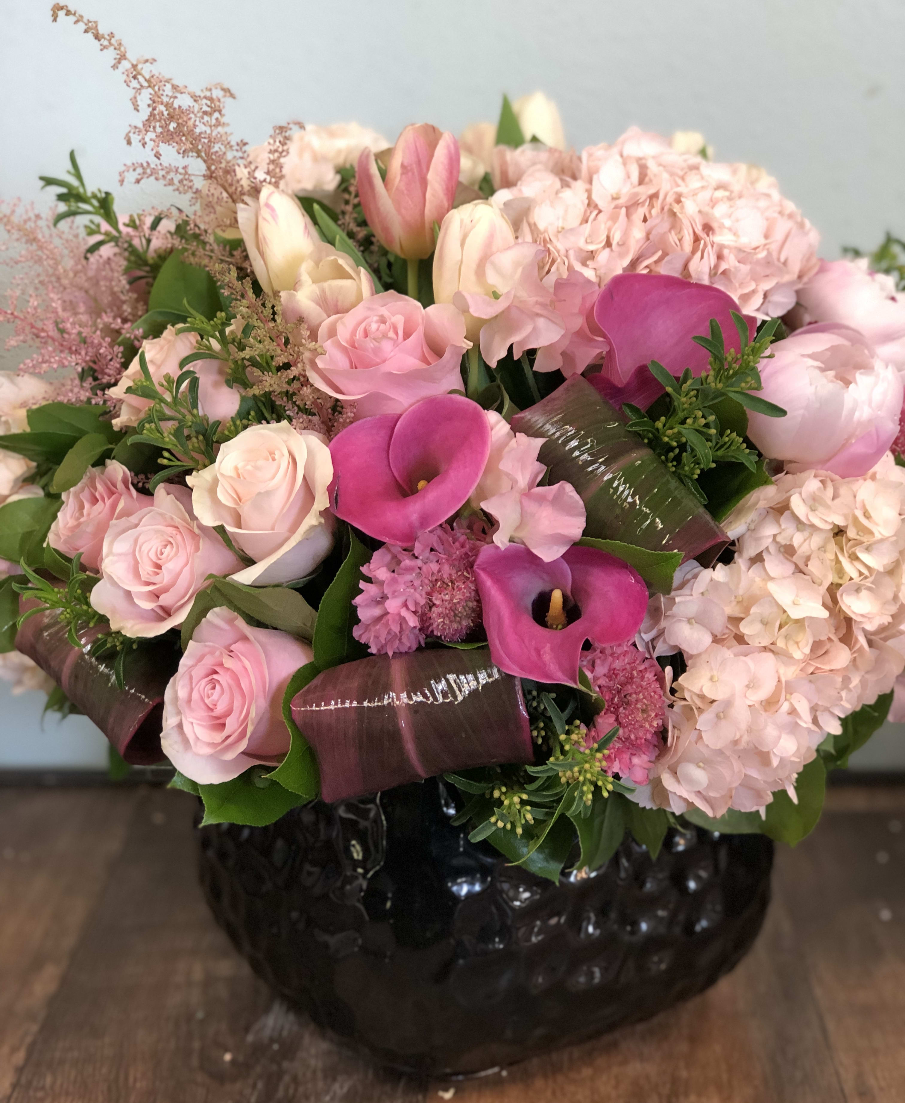 Rosa - Beautiful combination of Hydrangedas, Roses, Callas, Lisianthus and other seasonal flowers in different shades of pink arrangement in a black ceramic container. Flowers are subject to change due to seasonal availability, however we will create a similar arrangement.