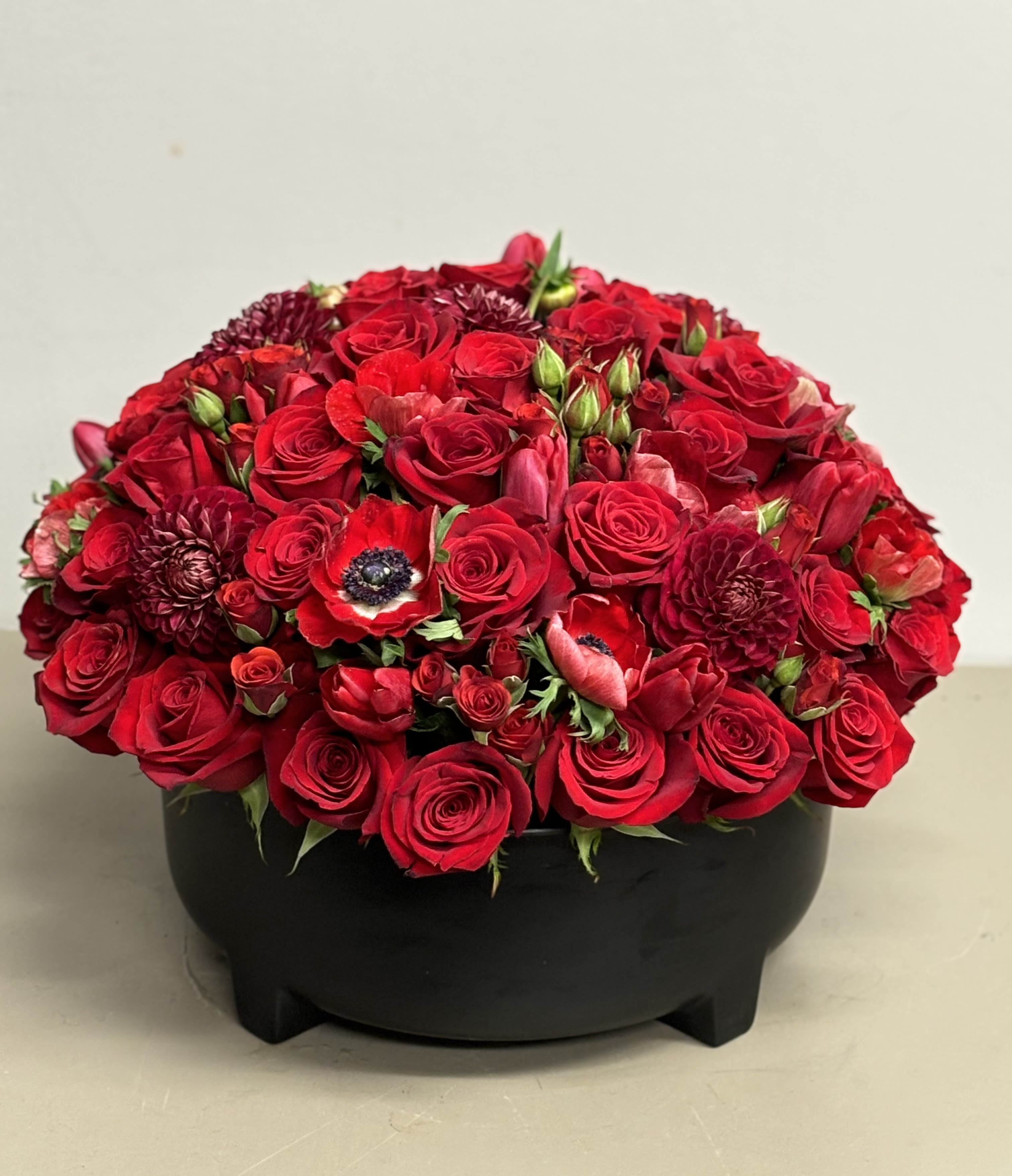 Red Beauty - Beautiful low &amp; lush combination of red Roses and other seasonal red flowers in a round ceramic container.