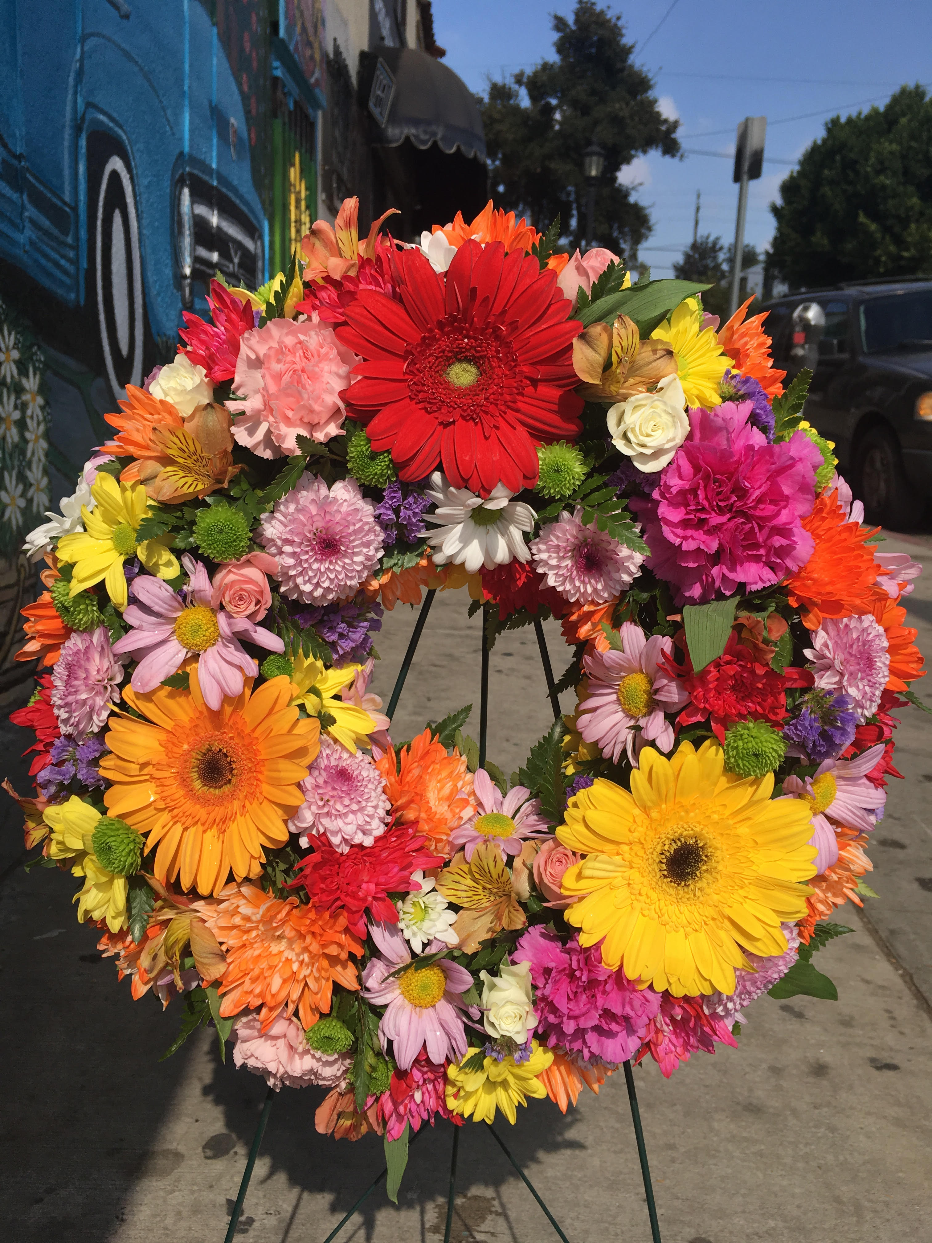 Spring Wreath - floral wreath arrangement, may include different spring flowers such as daisy,carnations, roses,gerberas daisy, foliage, wooden stand included.  *Order must be placed 2 - 3 days in advance* (Please note, same day pick-up or delivery is not available for this product) 