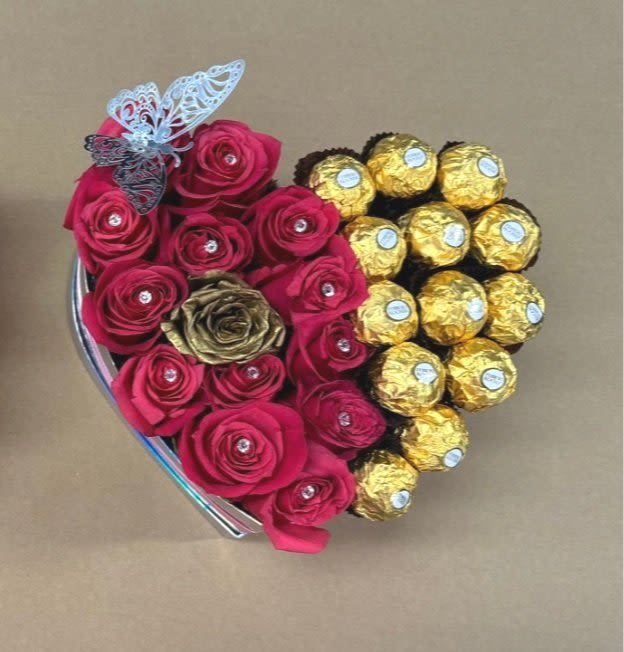 Sweetheart Delight – Heart-Shaped Bouquet with Fuchsia Pink Roses, Ferrero Rocher Chocolates & Metallic Silver Butterflies Sweetheart Delight – Heart-Shaped Bouquet with Fuchsia Pink Roses, Ferrero Rocher Chocolates & Metallic Silver Butterflies - Sweetheart Delight – Heart-Shaped Bouquet with Fuchsia Pink Roses, Ferrero Rocher Chocolates & Metallic Silver Butterflies Celebrate love and sweetness in the most unforgettable way with our Sweetheart Delight— a charming heart-shaped arrangement that blends vibrant blooms and delicious treats into one breathtaking gift. This dazzling design features half vivid fuchsia pink roses, symbolizing admiration, joy, and deep affection, paired with half luxurious Ferrero Rocher chocolates, wrapped in their signature gold foil for a rich, indulgent touch. Elegant metallic silver butterflies flutter throughout the arrangement, adding a graceful, shimmering accent that brings the entire design to life. All of this beauty is carefully presented in a heart-shaped container finished with a stylish bow, making it the perfect choice for anyone you want to impress and delight. Key Features: Half Fuchsia Pink Roses, Half Ferrero Rocher Chocolates Metallic Silver Butterfly Accents Heart-Shaped Container with Decorative Bow A Stunning Blend of Fresh Flowers and Gourmet Chocolates Perfect for: Anniversaries and Valentine’s Day Elegant gifts for loved ones Celebrating love, friendship, and special moments Gift a little magic, a lot of beauty, and a sweet surprise with Sweetheart Delight — a bouquet that's sure to leave a lasting impression.
