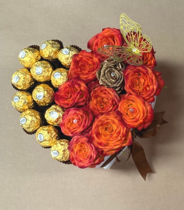 Sweetheart Delight – Heart-Shaped Bouquet with Orange Roses, Ferrero Rocher Chocolates & Metallic Butterflies Sweetheart Delight – Heart-Shaped Bouquet with Orange Roses, Ferrero Rocher Chocolates & Metallic Butterflies - Sweetheart Delight – Heart-Shaped Bouquet with Orange Roses, Ferrero Rocher Chocolates & Metallic Butterflies Celebrate love and sweetness in the most unforgettable way with our Sweetheart Delight — a charming heart-shaped arrangement** that blends fresh blooms and delicious treats into one stunning gift. This eye-catching design features half vibrant orange roses, bursting with warmth, enthusiasm, and joy, paired with half luxurious Ferrero Rocher chocolates, wrapped in their iconic gold foil for a rich, indulgent touch. Nestled among the blooms and chocolates are elegant metallic gold butterflies, adding a hint of whimsical sparkle and magic to the arrangement. Everything is beautifully presented in a heart-shaped container adorned with a stylish bow making it the perfect romantic or celebratory gesture. Key Features: Half Orange Roses, Half Ferrero Rocher Chocolates Metallic Gold Butterfly Accents Heart-Shaped Container with Decorative Bow A Unique Blend of Fresh Flowers and Gourmet Chocolates Perfect for: Anniversaries and Valentine’s Day Thoughtful gifts for loved ones Celebrations of love, friendship, and special milestones Gift a little magic and a lot of love with Sweetheart Delight— a bouquet that's as sweet as it is beautiful.