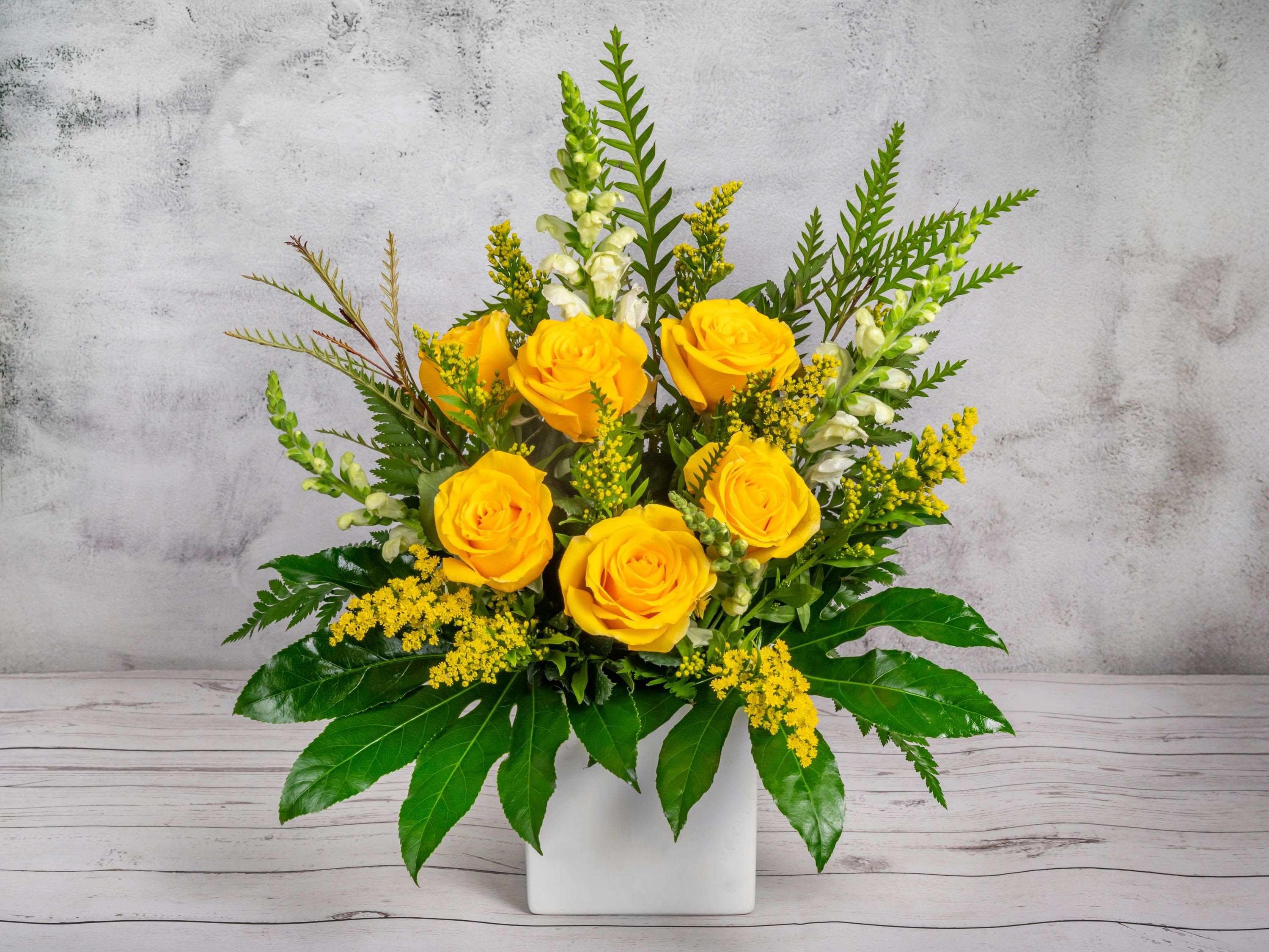 Just Bright Just Bright - Add a burst of sunshine to any occasion with this radiant yellow rose arrangement! Featuring six vibrant yellow roses paired with delicate white snapdragons, golden solidago, and lush greenery, this bouquet is designed to bring joy and warmth. Displayed in a modern white ceramic cube vase, it offers a sleek and stylish presentation that’s perfect for brightening someone’s day, celebrating achievements, or simply uplifting your space.