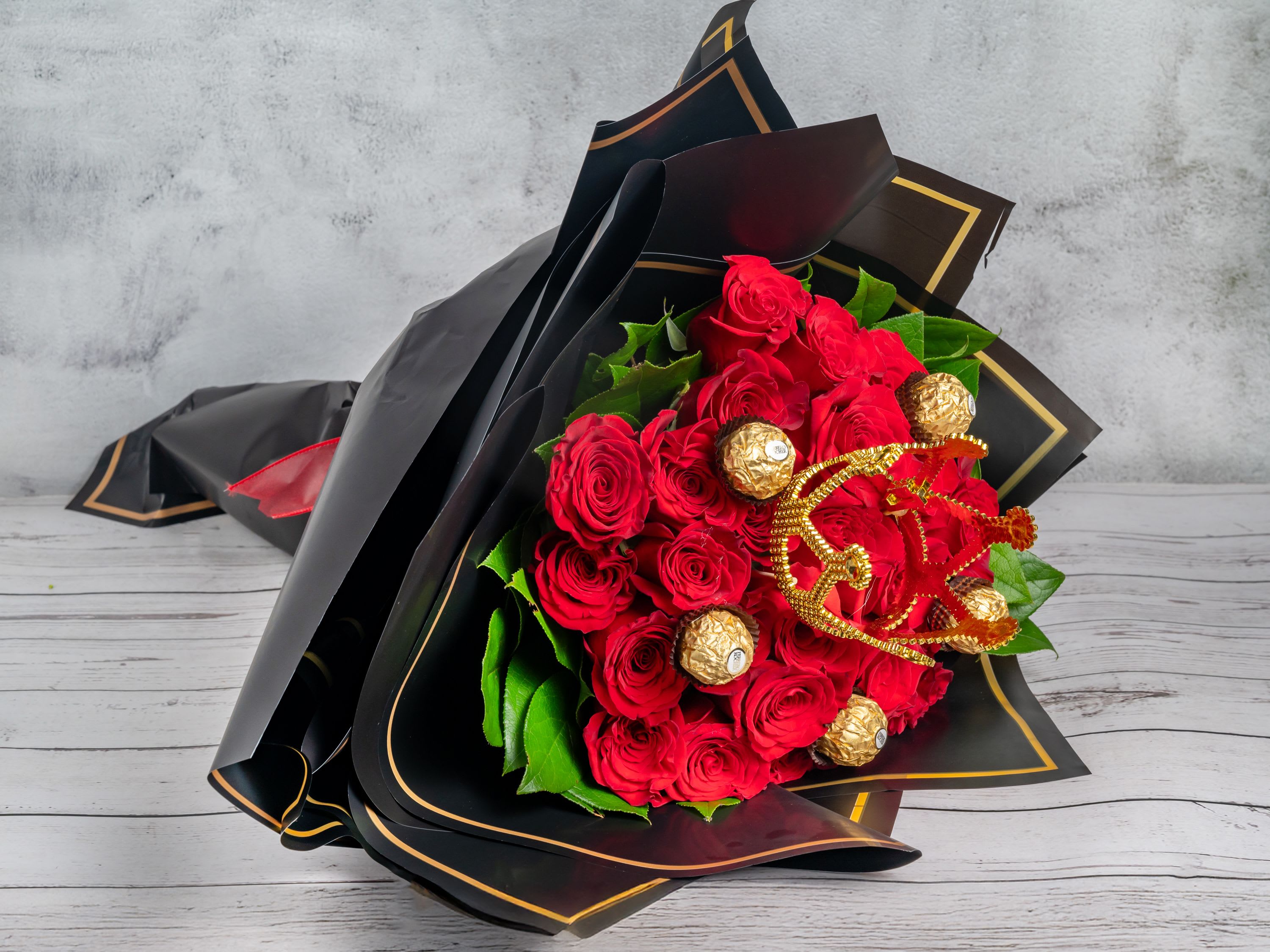 Royal Indulgence Royal Indulgence - A luxurious arrangement of 24 bold red roses, accented with rich green foliage and adorned with indulgent gold-wrapped chocolates. Elegantly wrapped in sleek black paper with gold trim, this bouquet makes a statement of opulence and grandeur. Perfect for romantic gestures, special celebrations, or when you want to show appreciation in the most decadent way. Make any moment unforgettable with this exquisite gift.